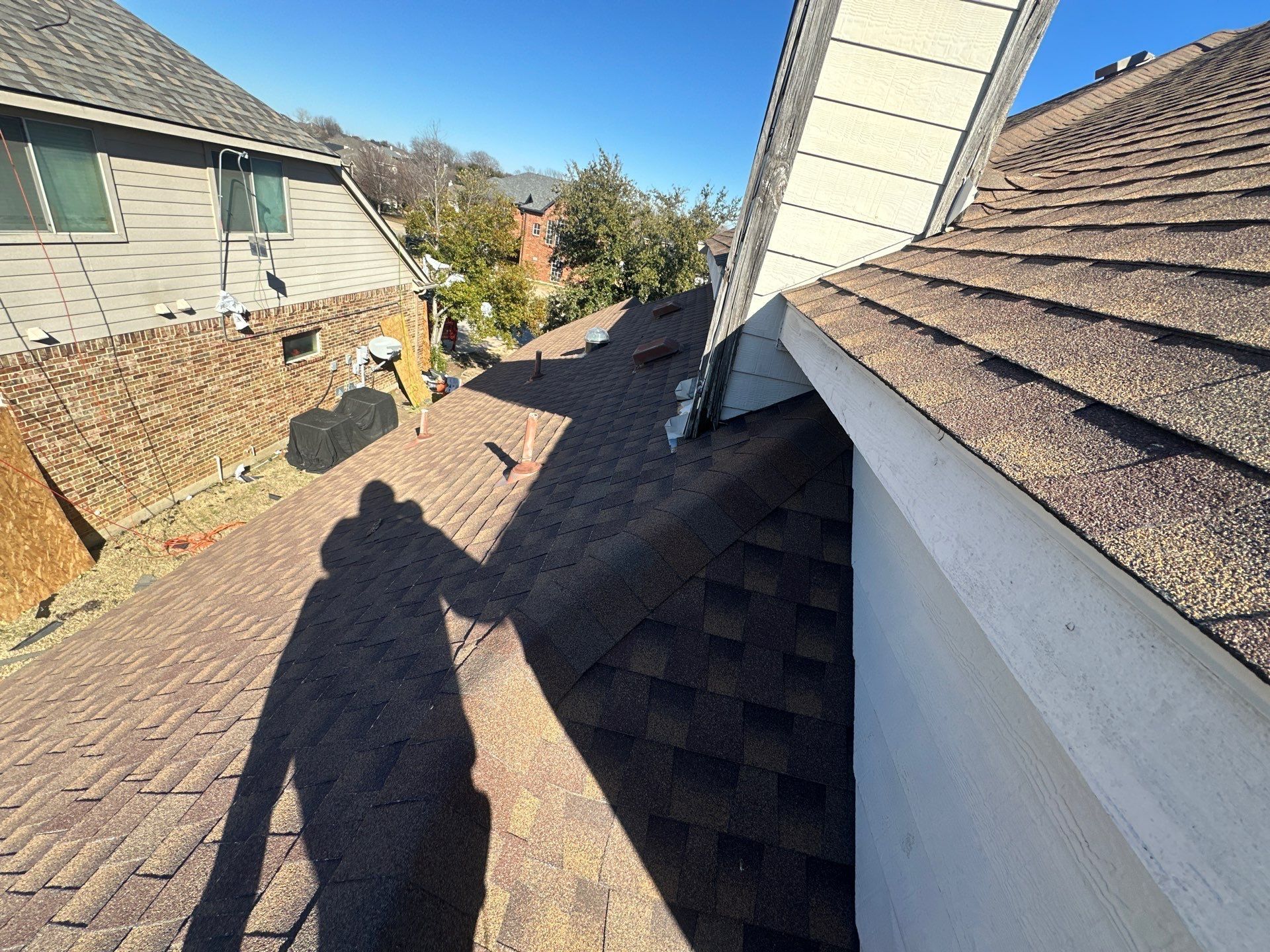 Roof walkway between houses with shingles, siding, and a person’s shadow in sunlight.