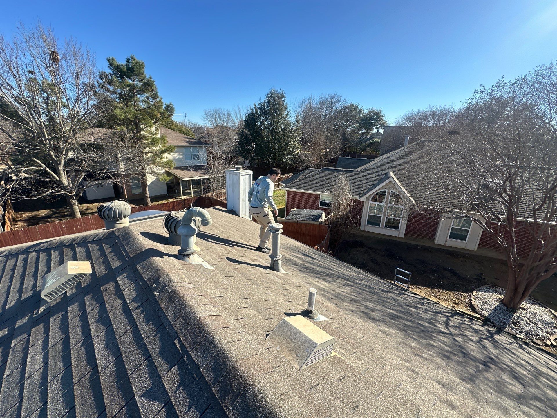 Rooftop with two workers and vents, overlooking houses and trees on a sunny day