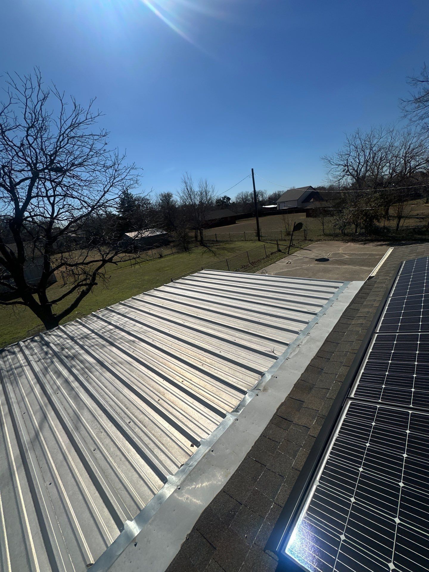 Rooftop with white corrugated panels beside solar panels under a clear blue sky.