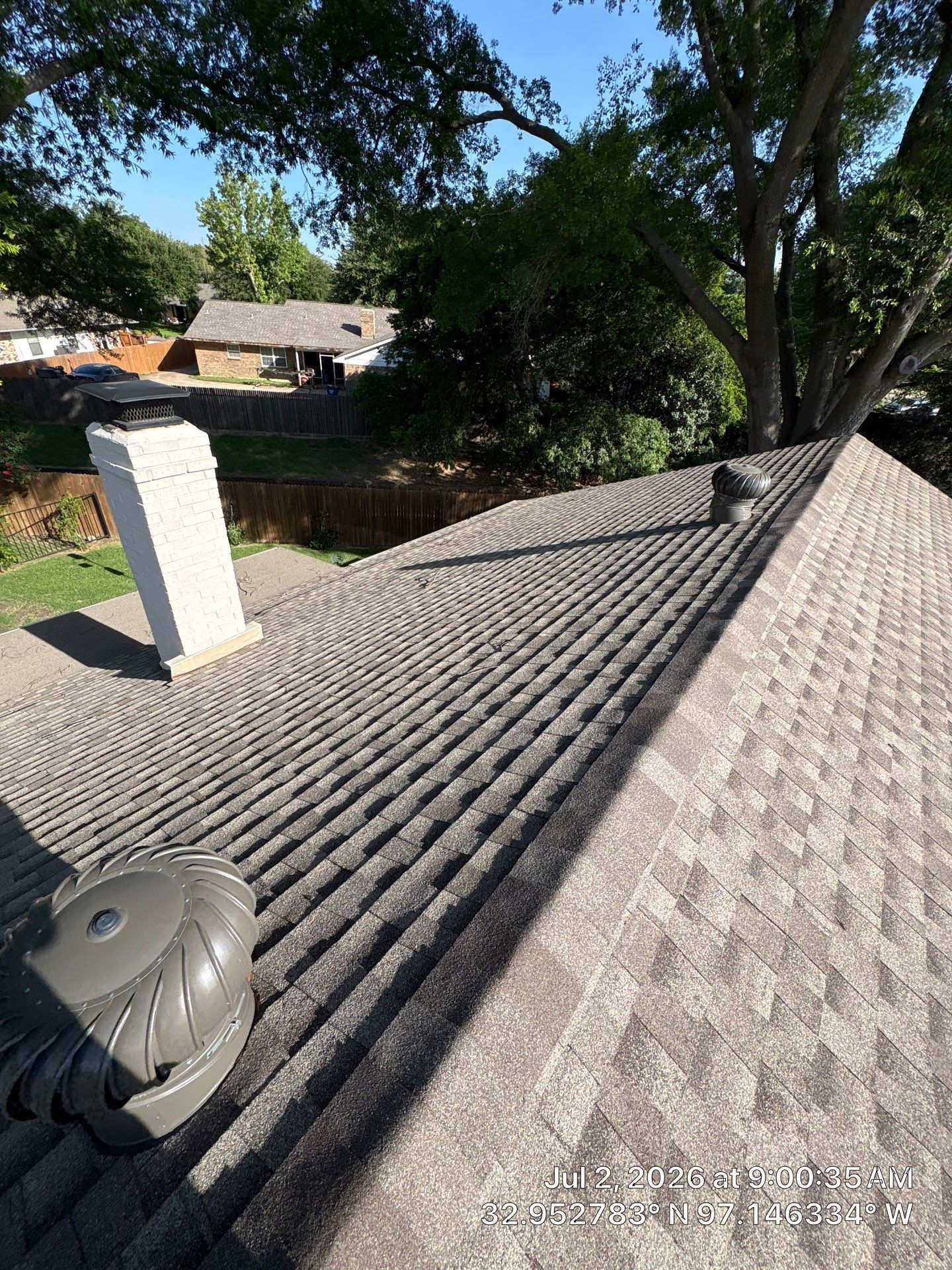 Rooftop with textured shingles, vents, and large trees overlooking neighboring houses.