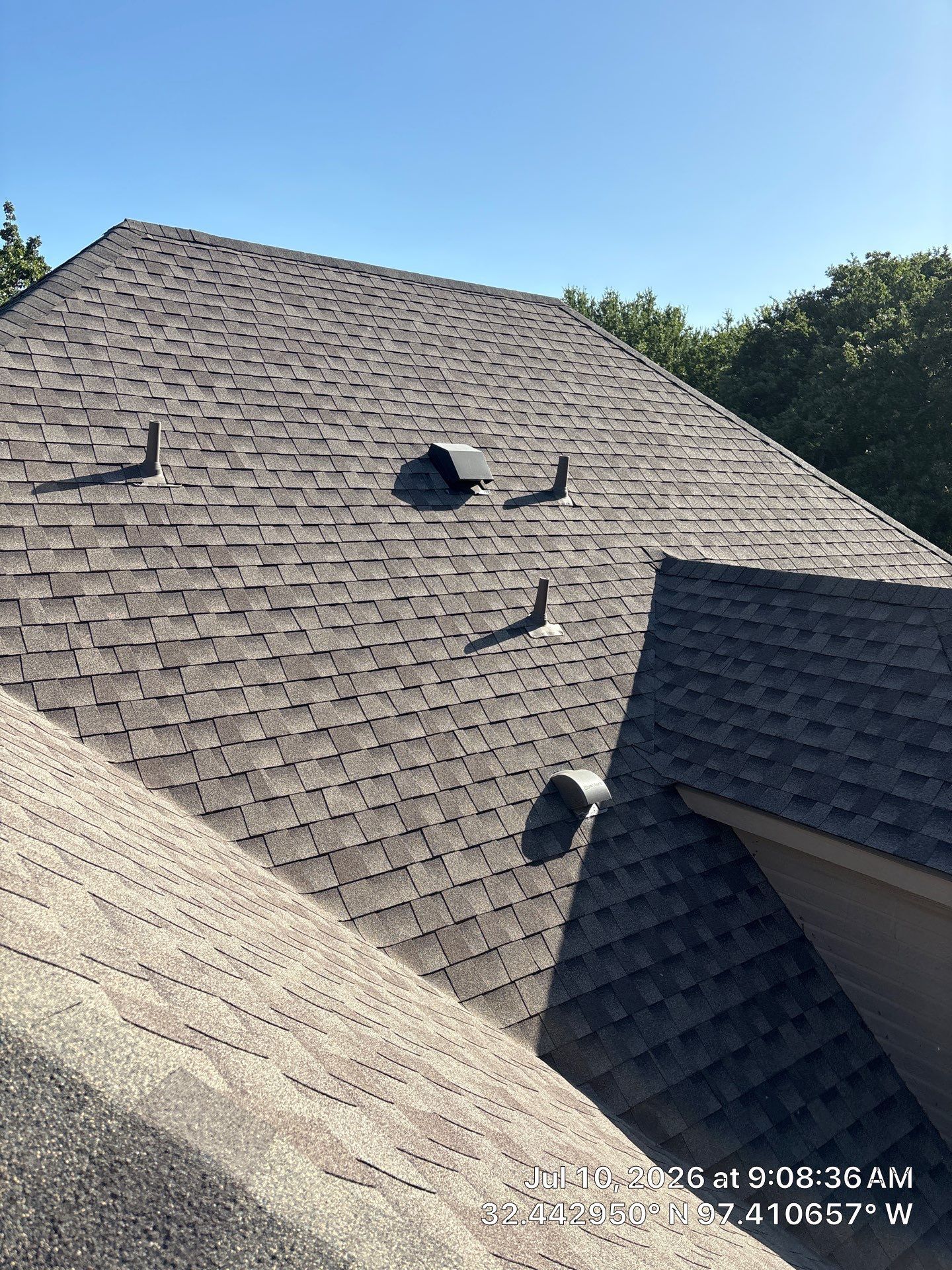 Gray shingle roof with several damaged vents and a patch of shadow under a clear blue sky