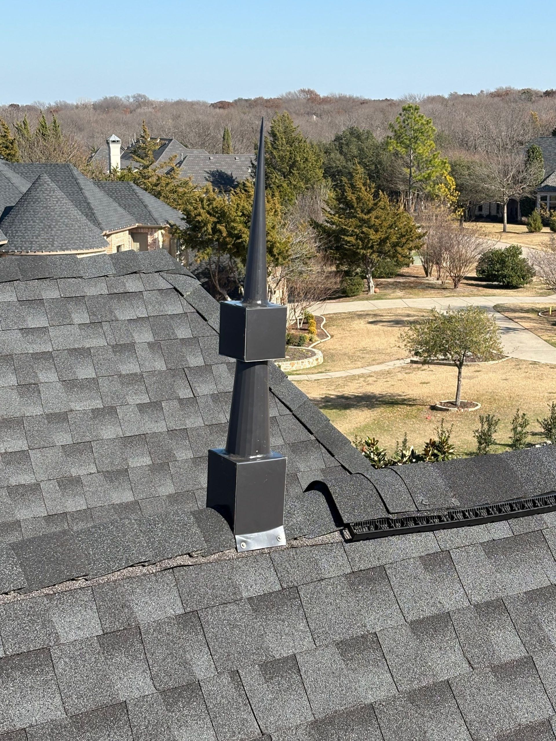 Rooftop vent pipe and shingles overlooking a dry suburban landscape and trees.