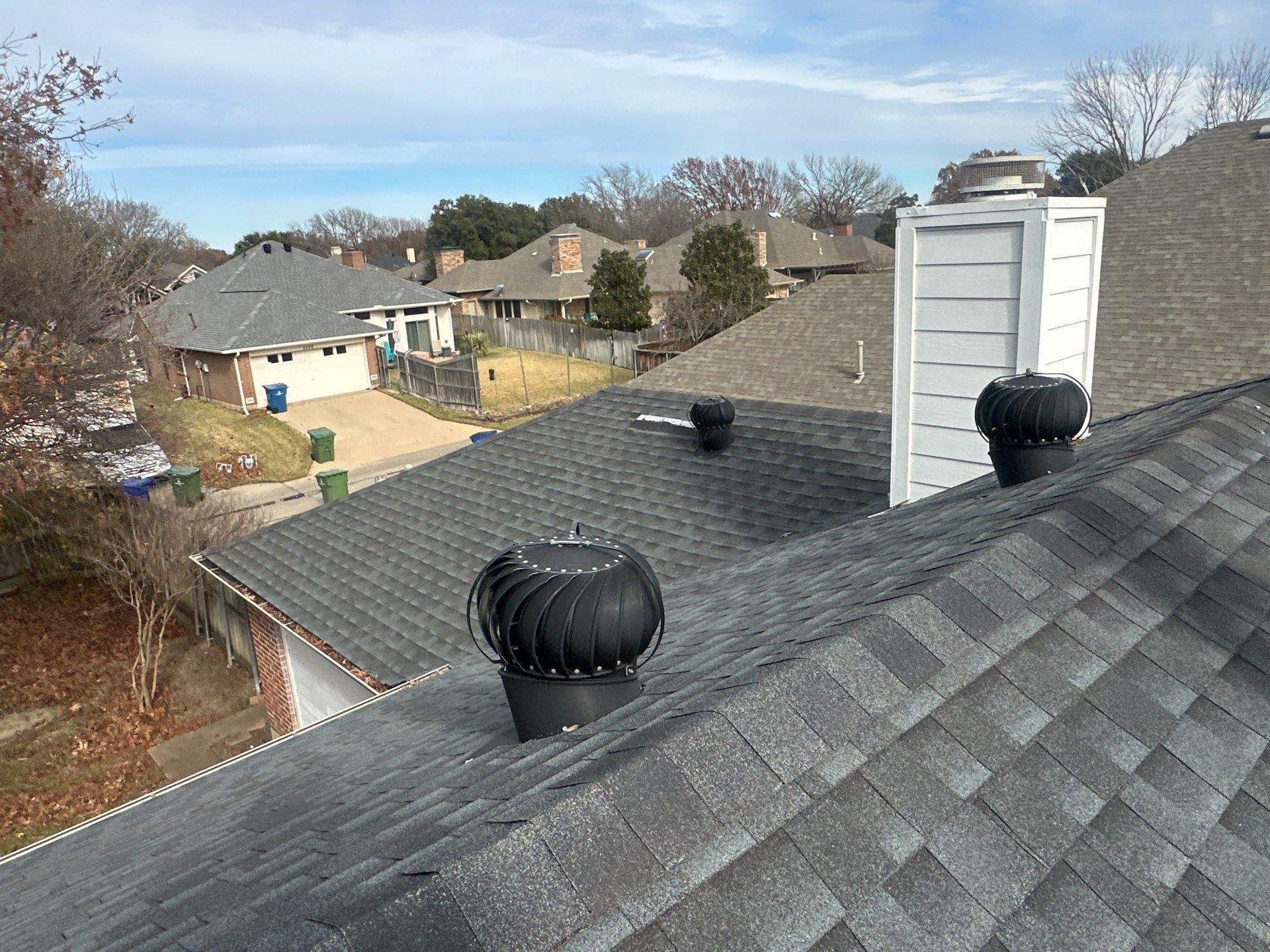 Rooftops with black turbine vents overlooking suburban houses and leafless trees on a clear day