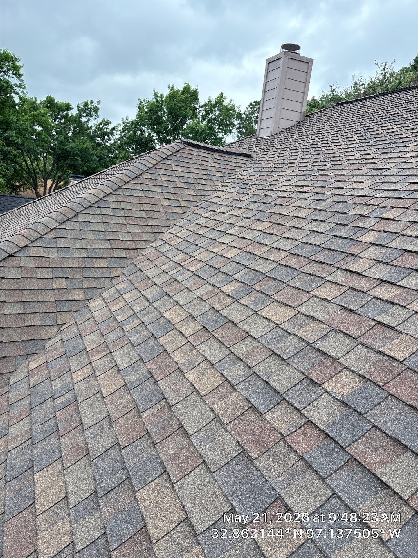 Shingled sloped roof with a chimney and trees in the background