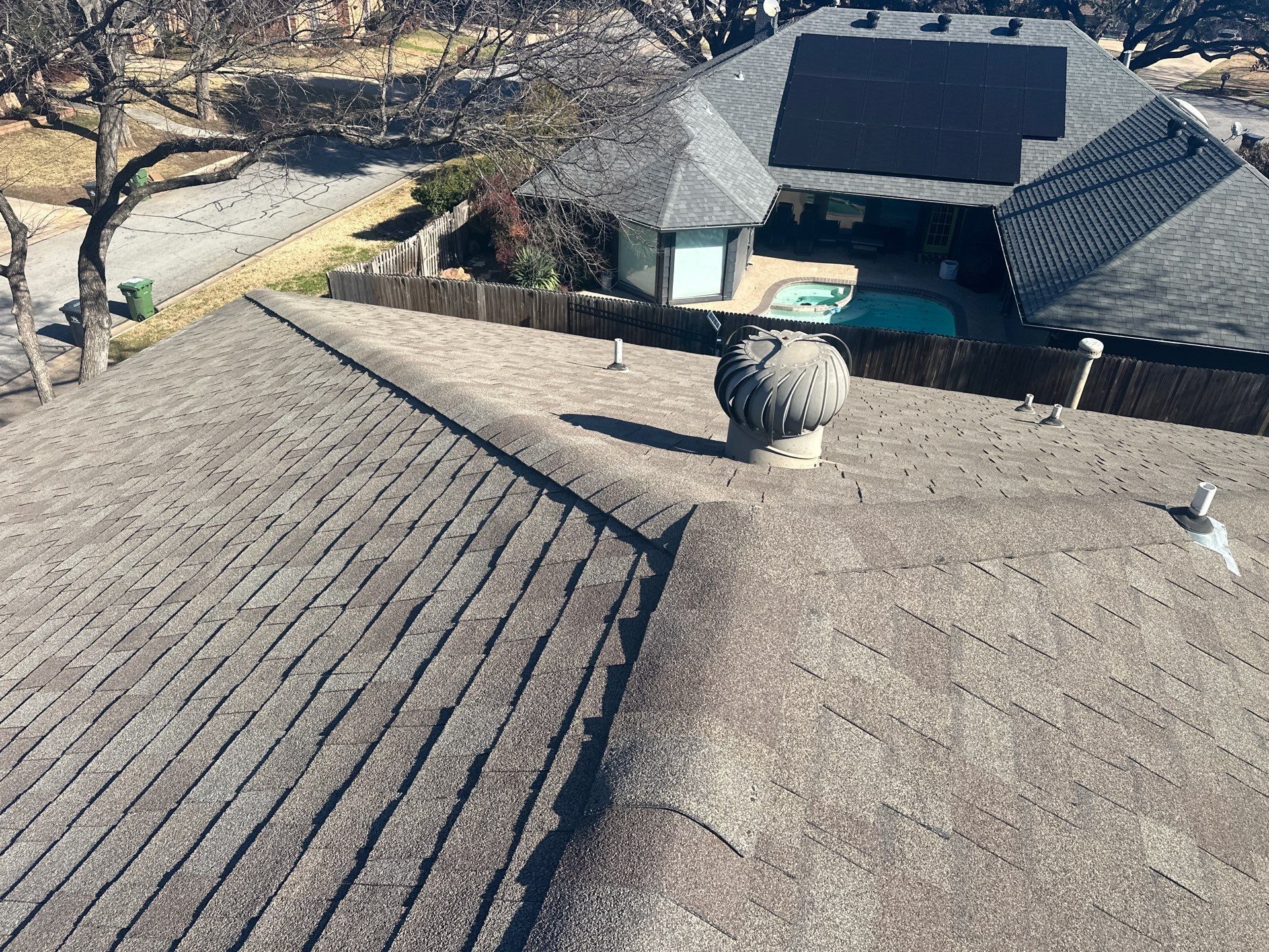 Rooftop with gray shingles, a vent chimney, and trees along a creek in the background