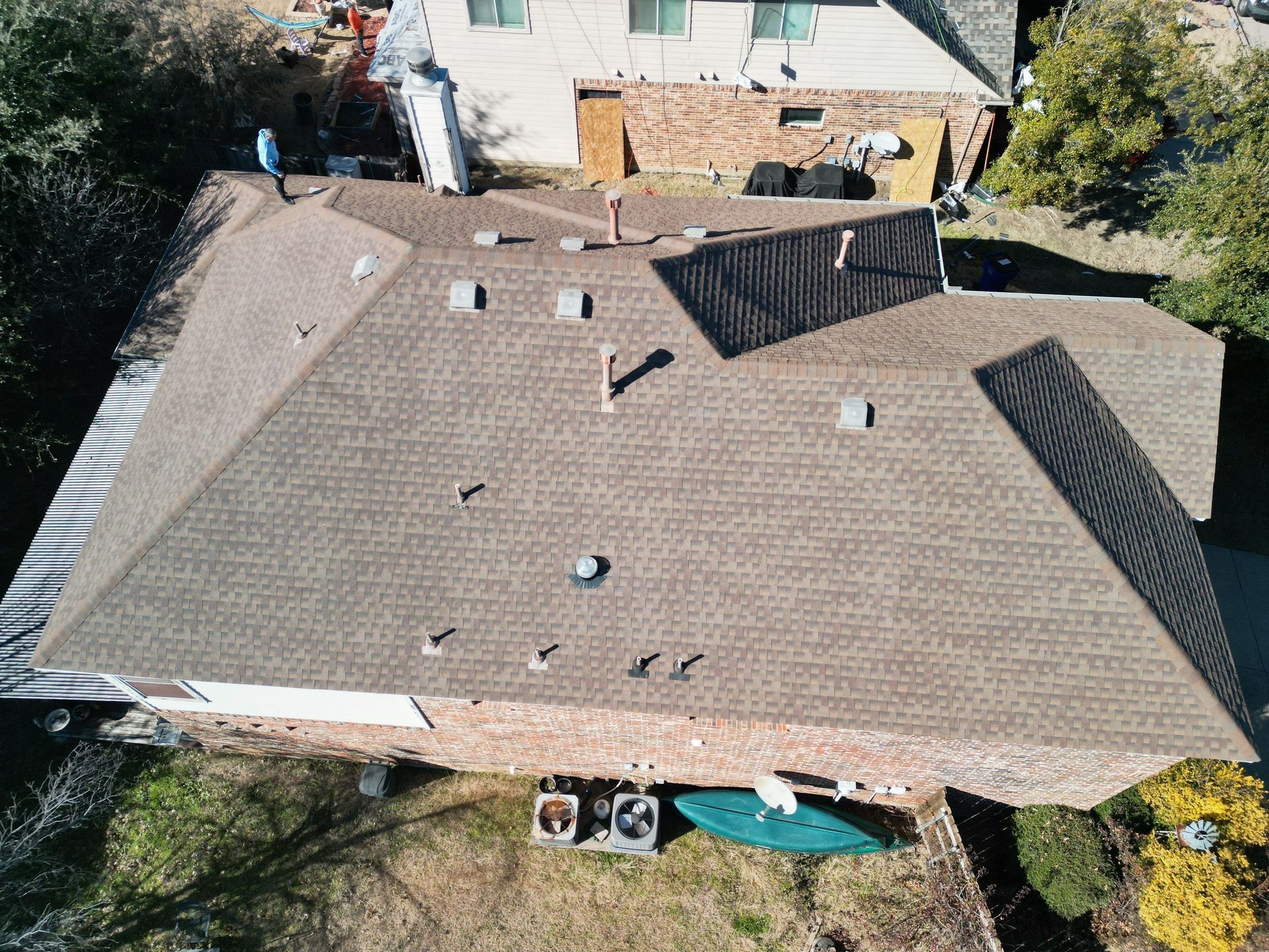 Aerial view of a house roof with shingles, skylights, and a small yard with a canoe below.