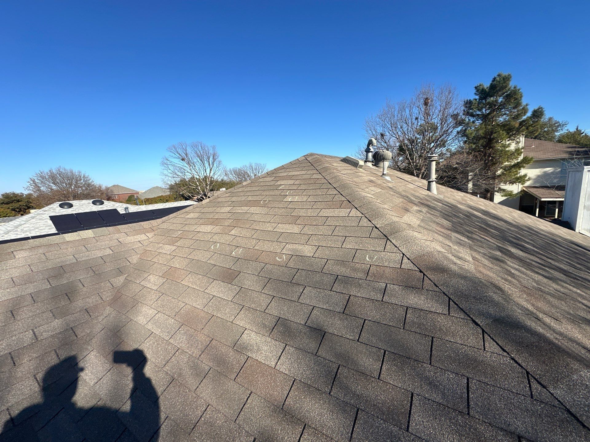 Shingled rooftop with two people’s shadows under a clear blue sky in a suburban neighborhood