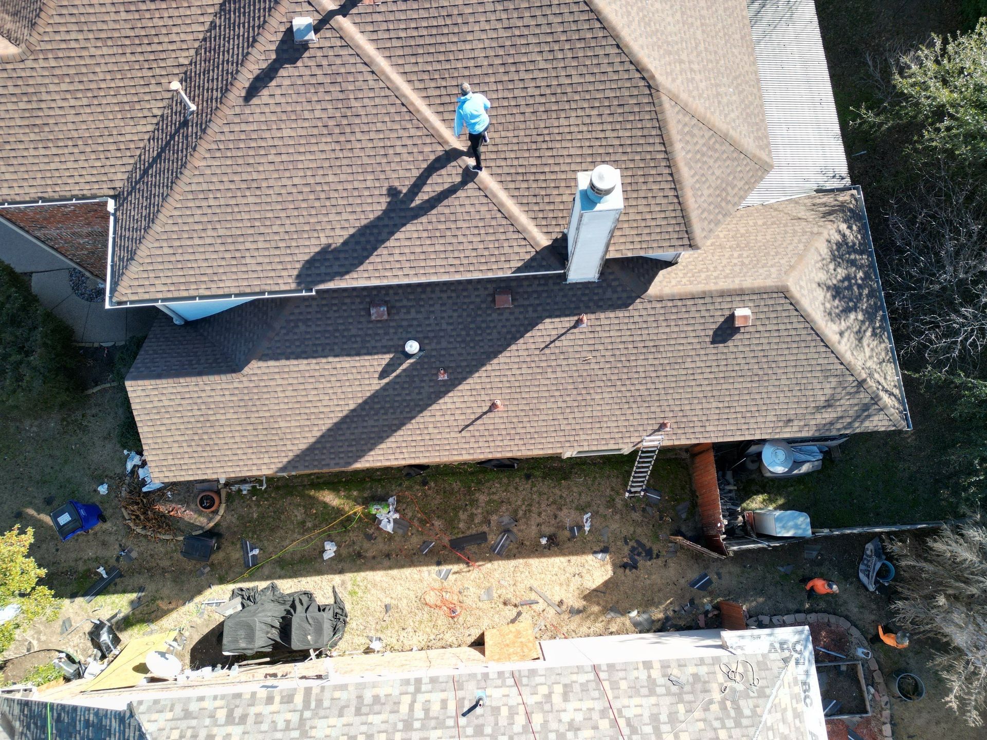 Aerial view of a roof with two workers and construction materials beside the house.