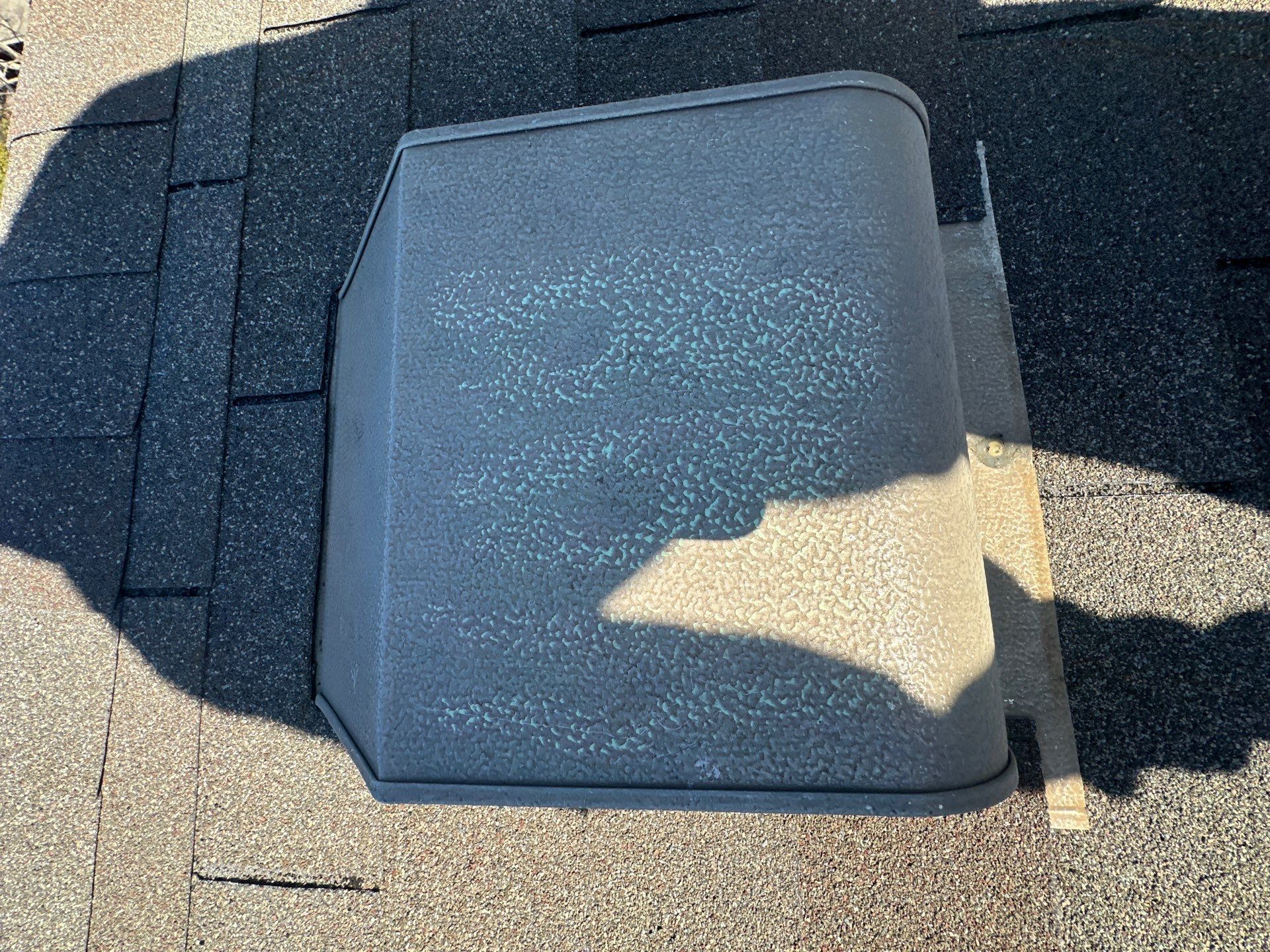 Roof skylight hatch on gray shingle roof in sunlight