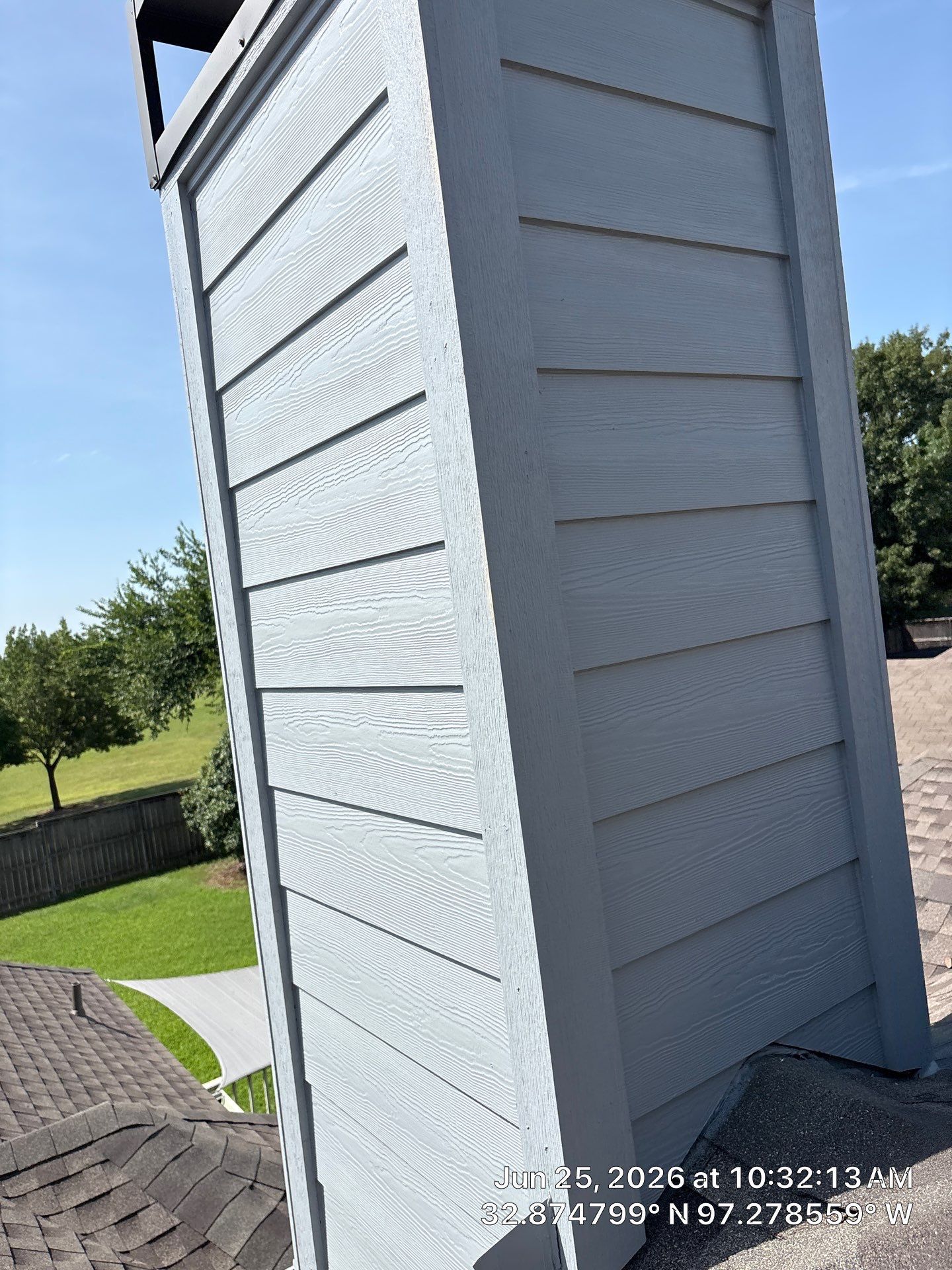 White house siding with vertical trim beside a shingled roof and green yard under a clear blue sky
