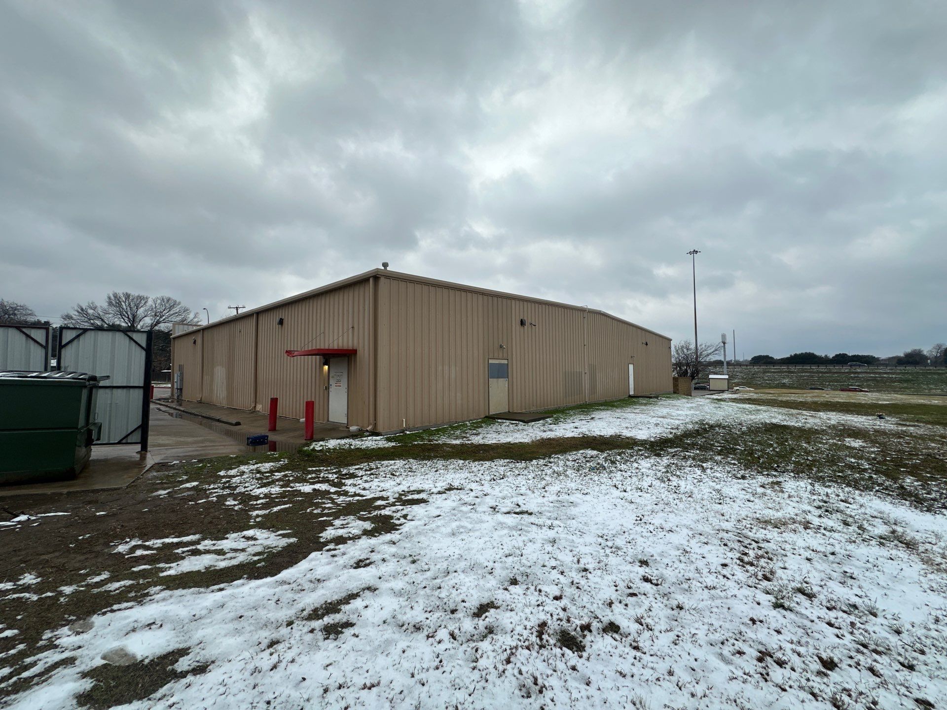 Tan warehouse building on a snowy, open lot under a cloudy sky