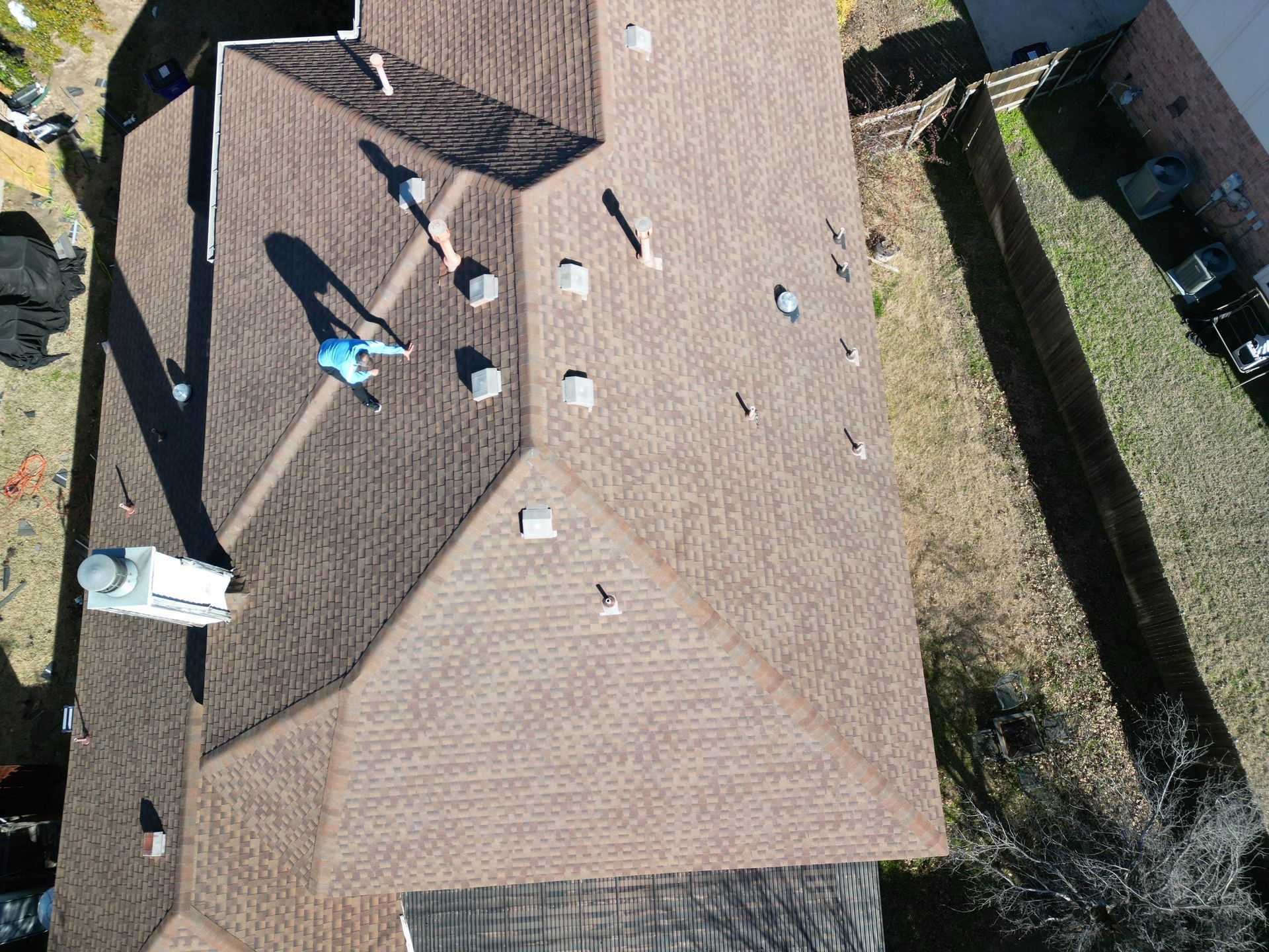 Aerial view of a tan house roof with two workers and scattered roofing equipment.