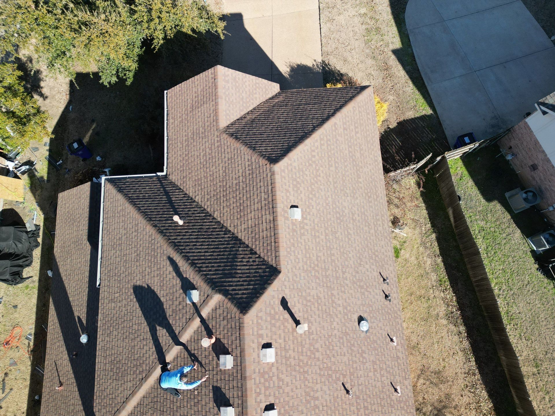 Aerial view of a house roof with skylights and two people on the deck by a backyard fence.