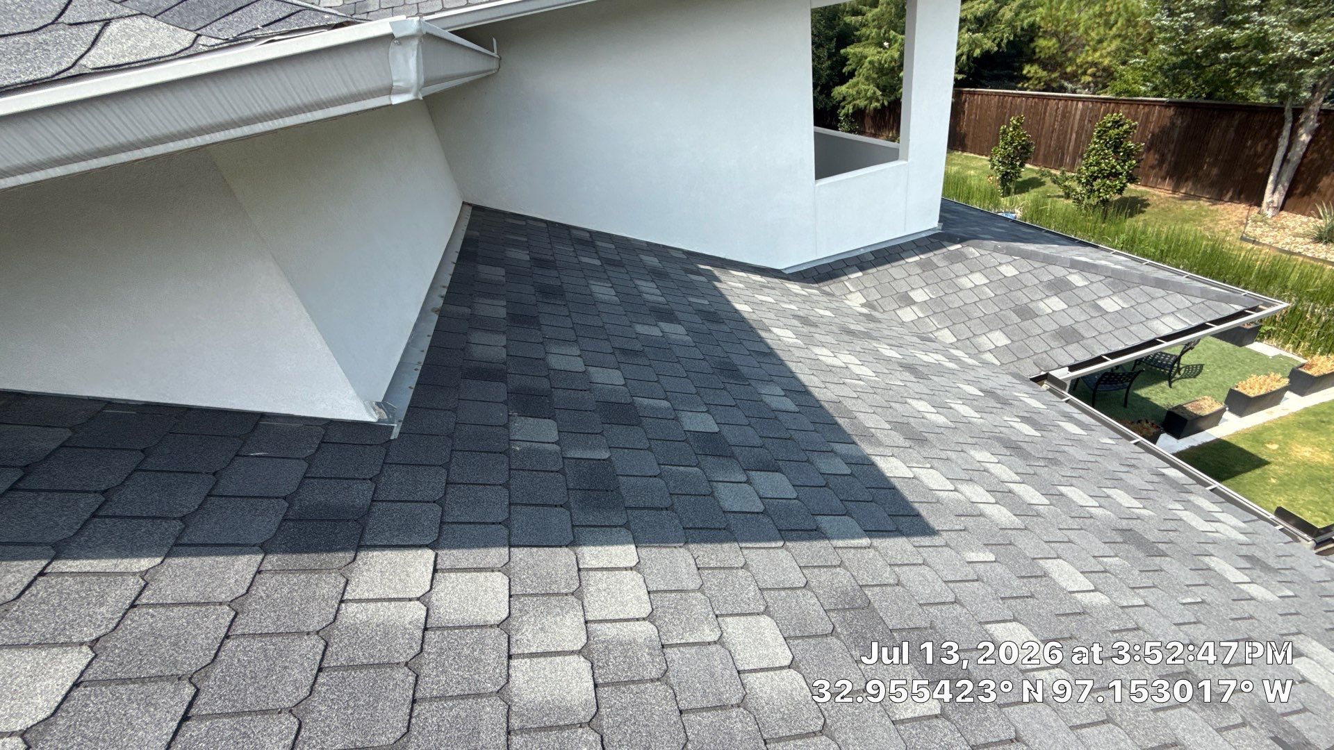 Gray paver patio beside a white house wall, with a small garden bed and lawn edge.
