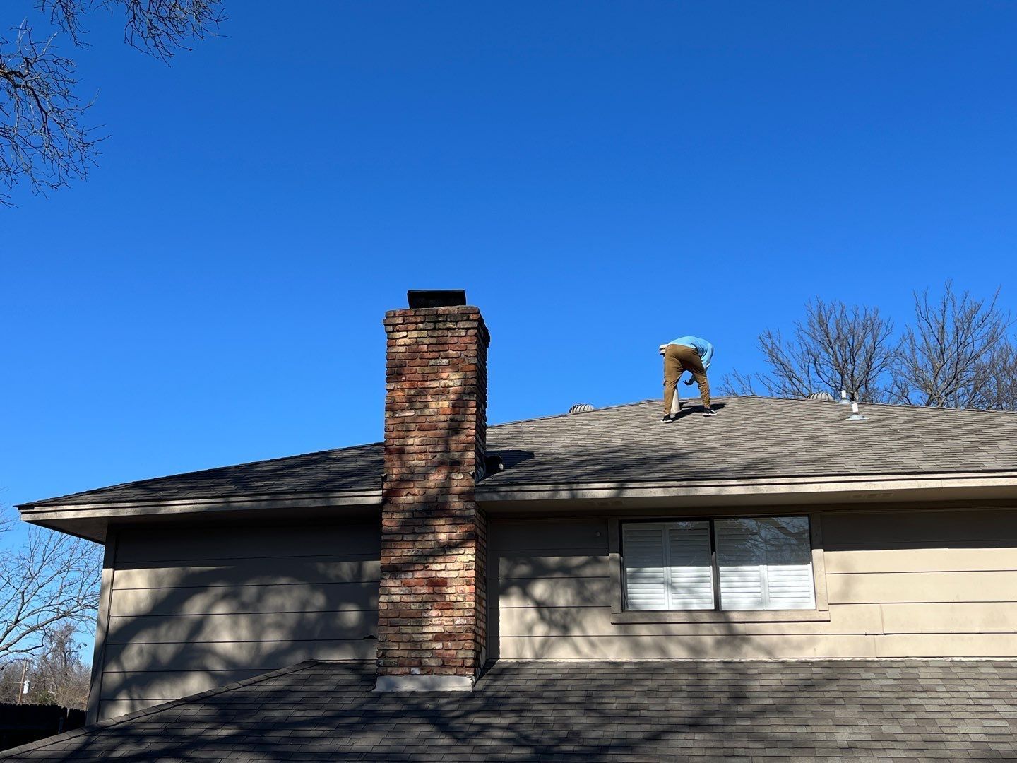 House roof with chimney and a small animal standing near the ridge under a clear blue sky