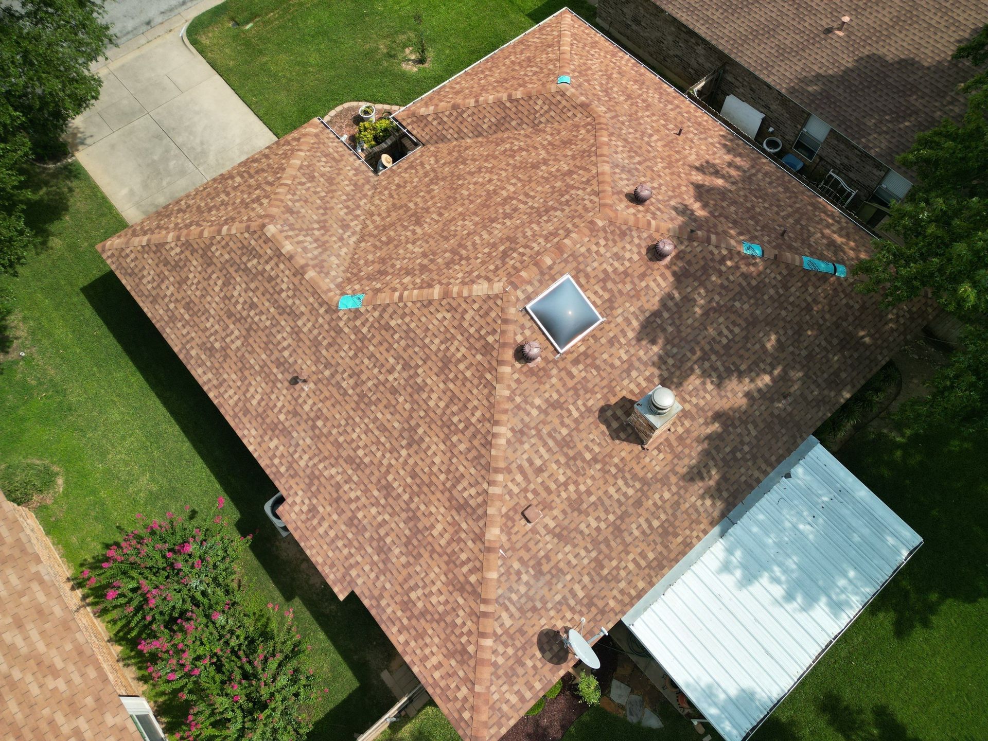 Aerial view of a house with a red-tiled roof, skylight, vents, and surrounding green lawn.
