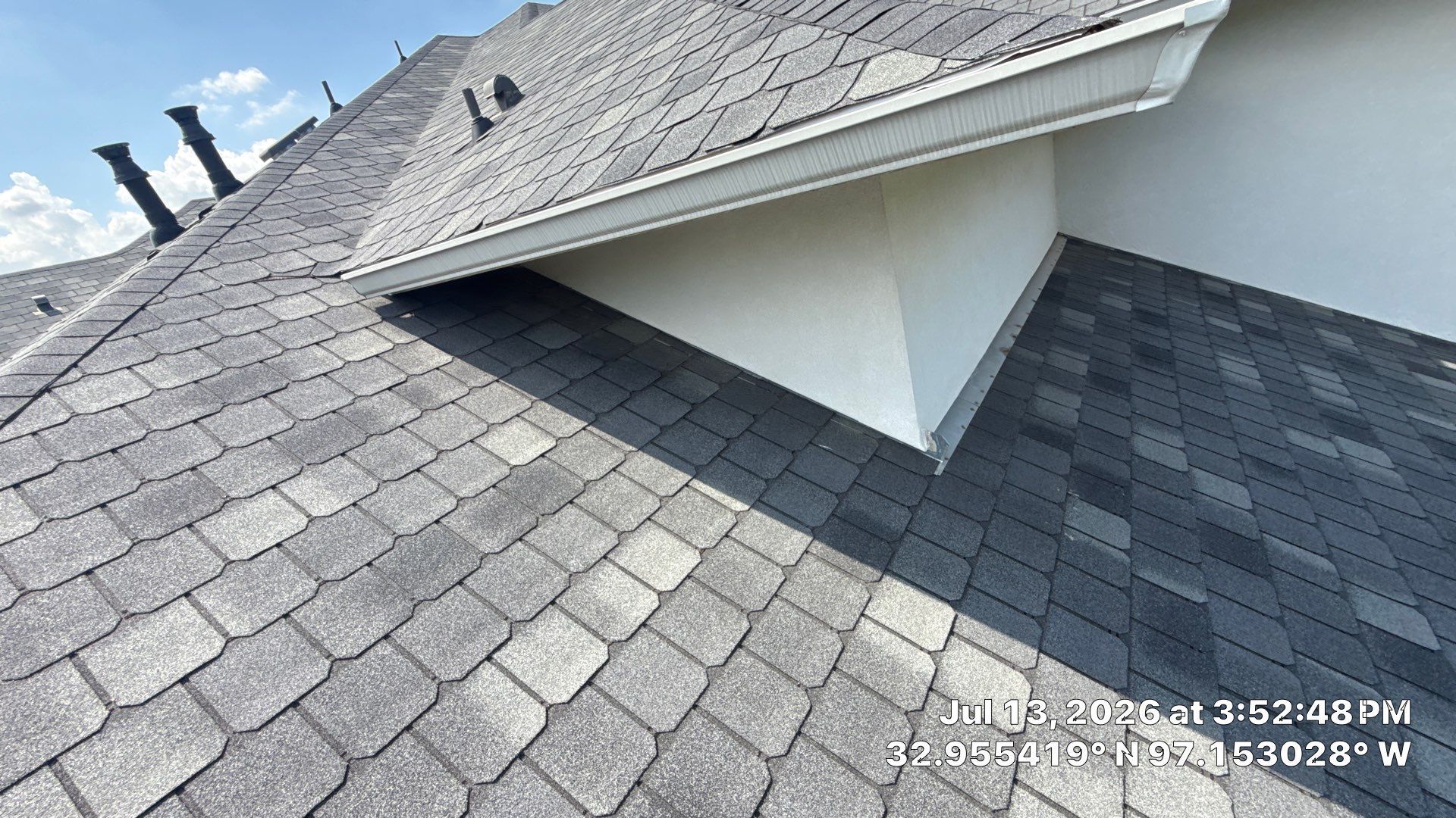 Rooftop skylight vent on gray shingle roof, with white trim and one open panel casting a shadow.