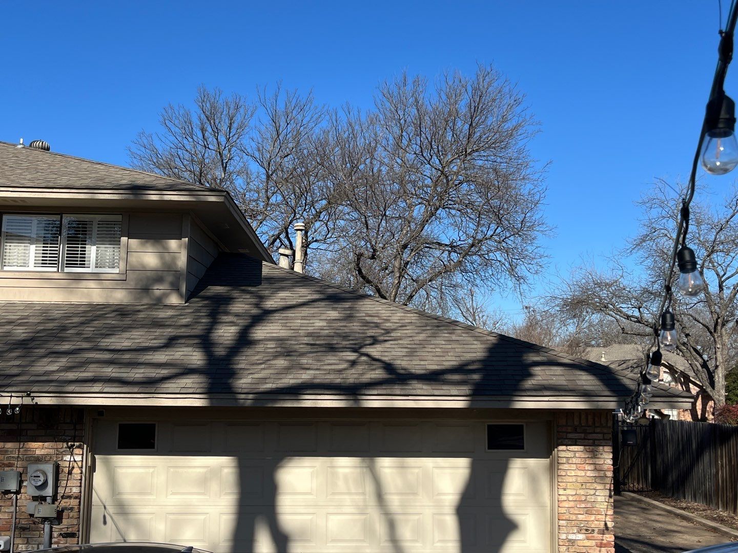 Suburban house with beige garage and leafless trees under a clear blue sky