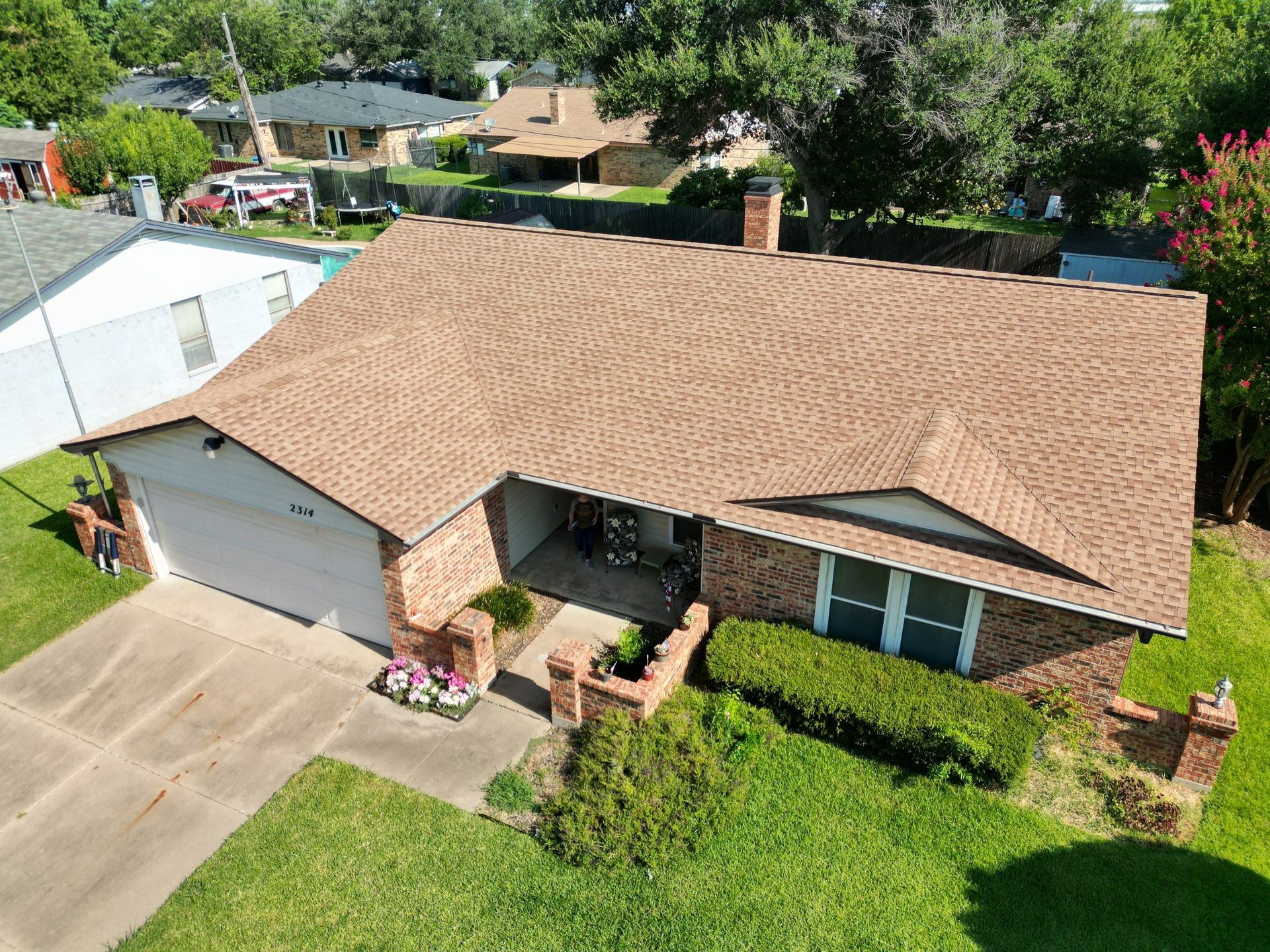 Aerial view of a suburban house with tan roof, driveway, and green lawn