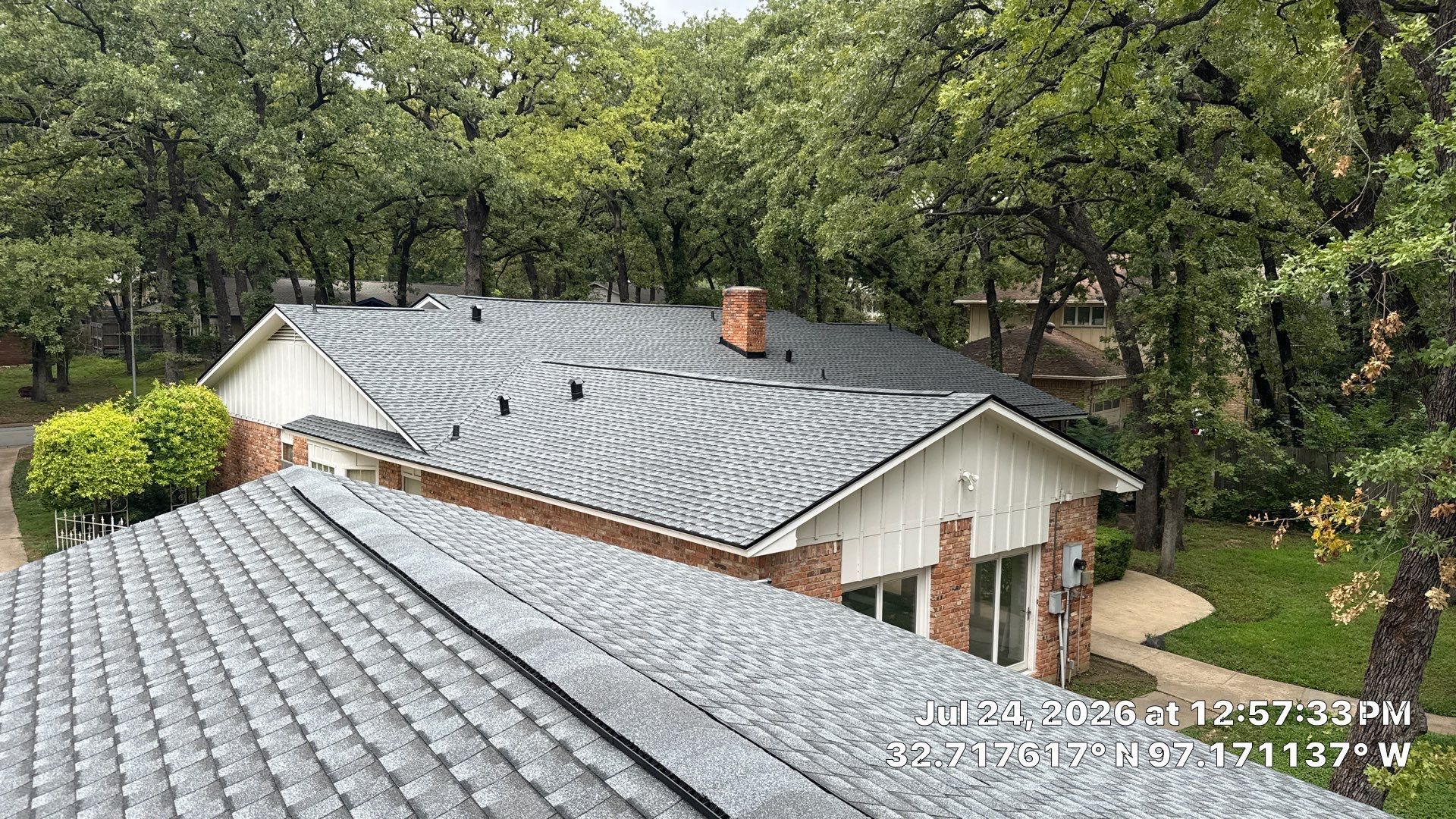 Aerial view of a house with gray shingle roof surrounded by trees and greenery.