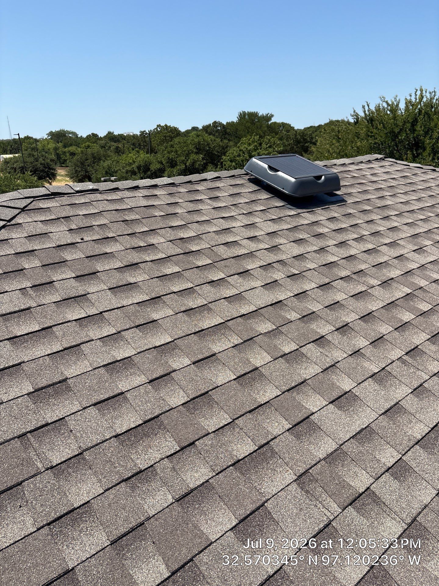 Rooftop with gray shingles and a black roof vent under a clear blue sky