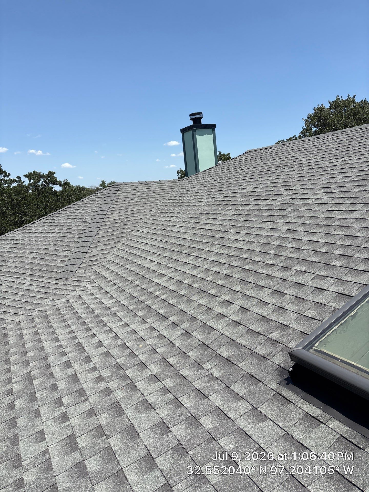 Gray shingled roof with a chimney and skylight under a clear blue sky