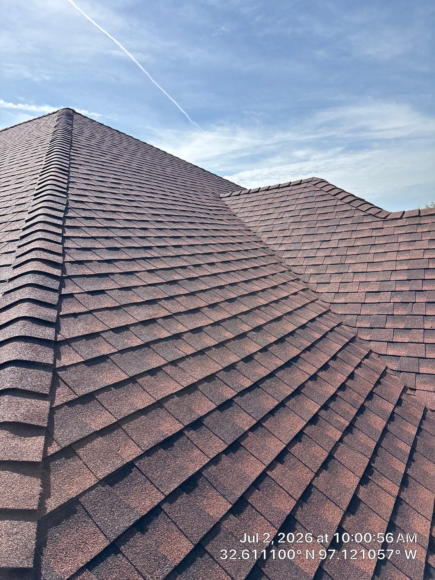 Brown shingled rooftops beneath a blue, lightly clouded sky