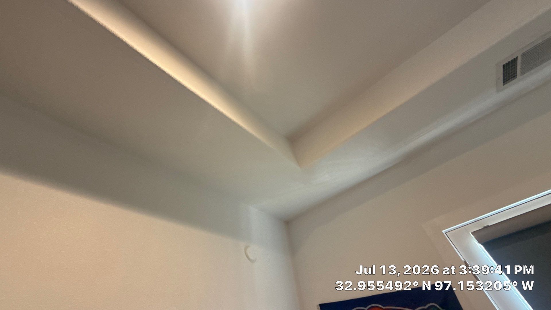 Corner of a white room ceiling with a vent and a faint timestamp overlay in the lower right.