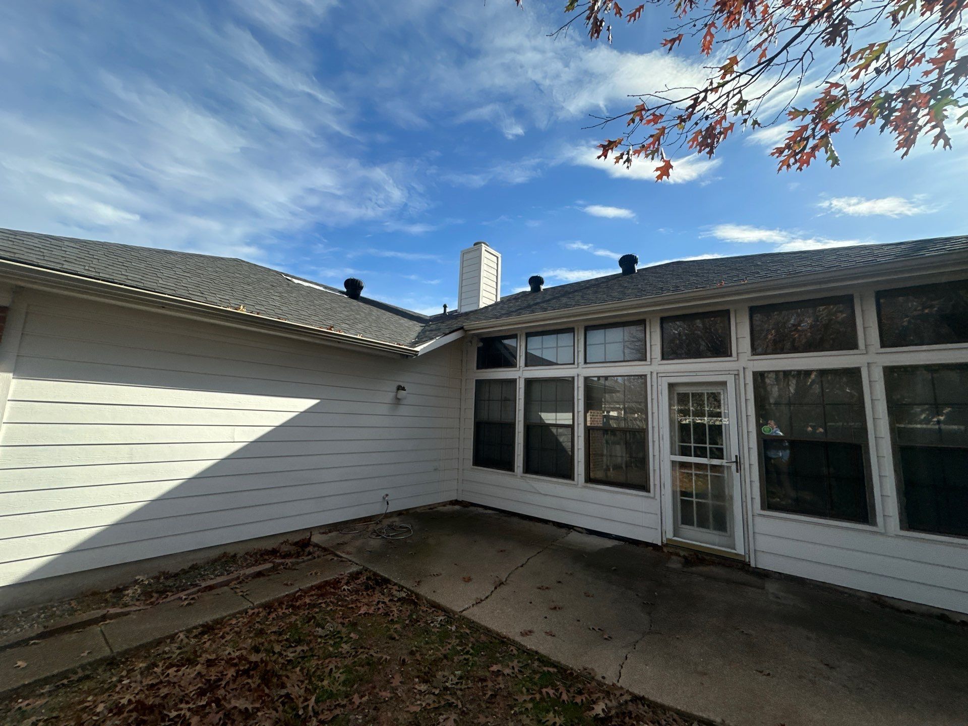 White house exterior with a small concrete patio, sliding windows, and a blue sky with tree branches