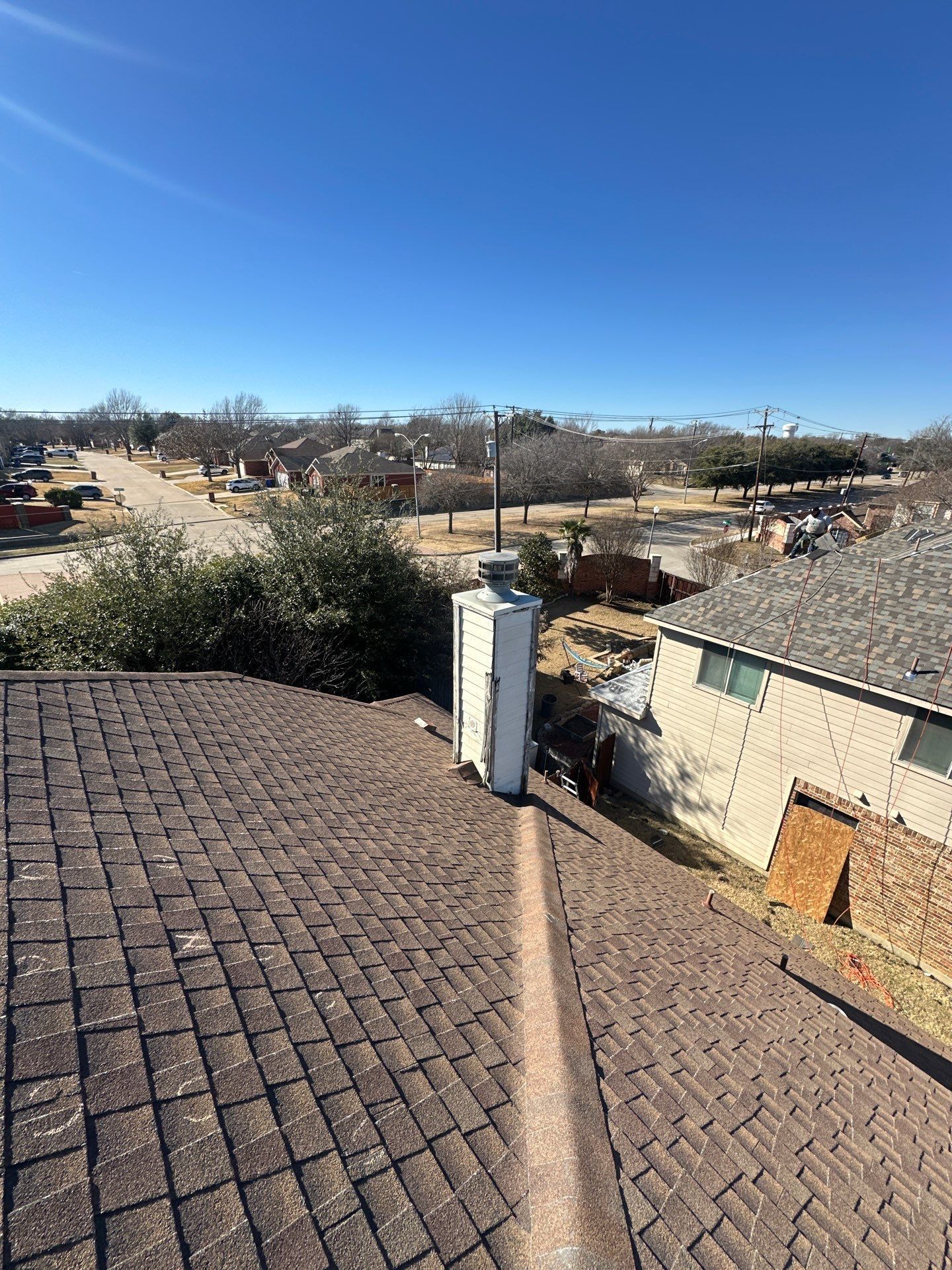 Rooftop view over a suburban neighborhood under a clear blue sky, with houses and trees below