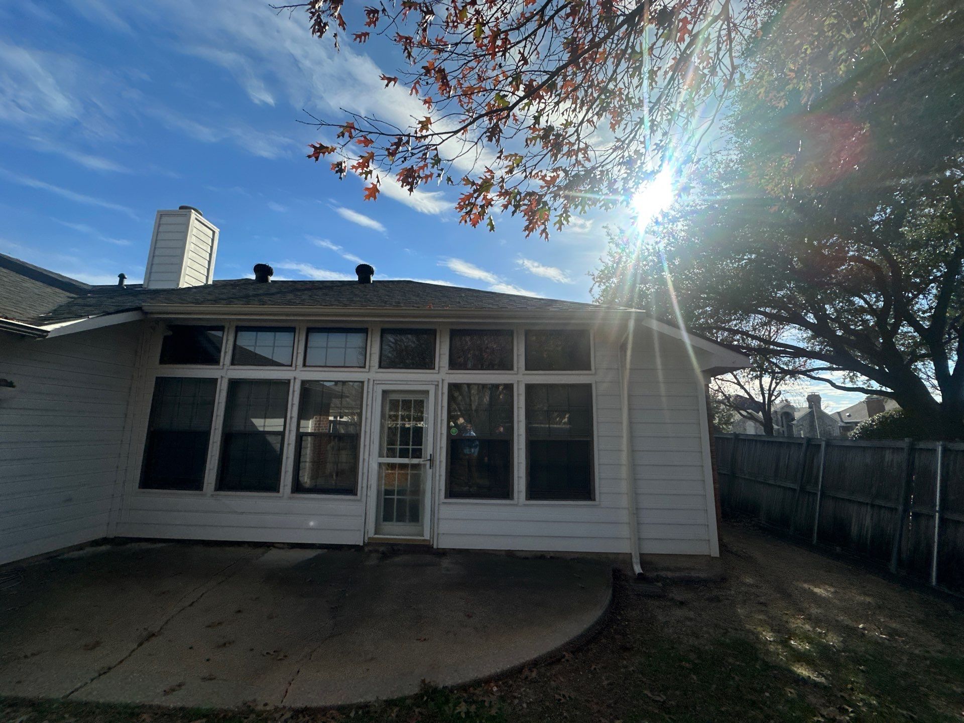 Small white house with a screened porch, bright sun, and a large tree in the yard