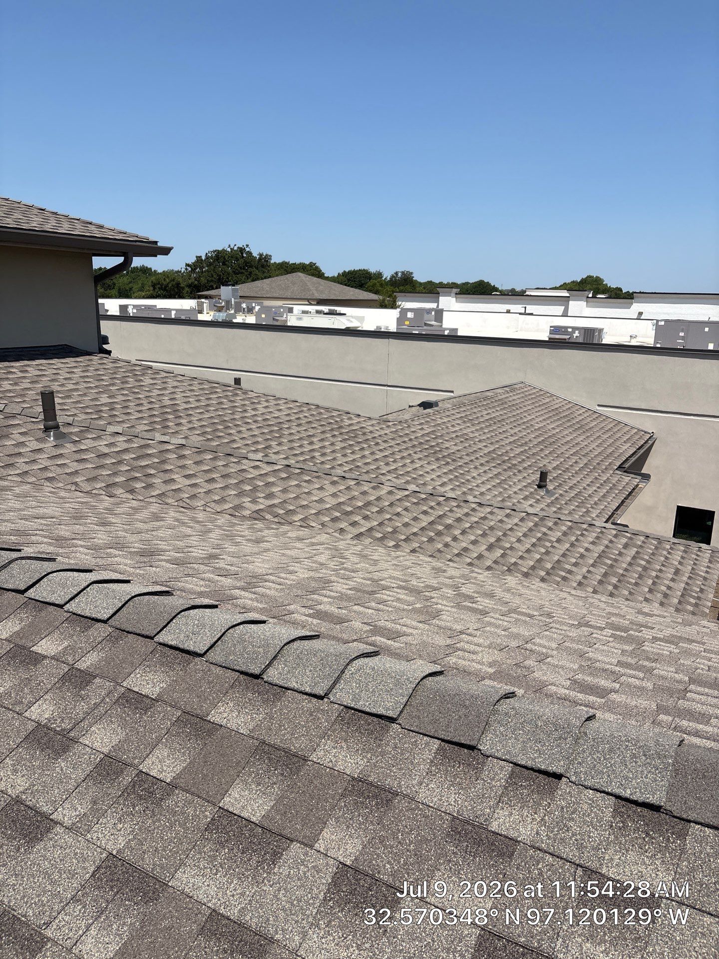 Residential rooftops with gray shingles under a clear blue sky.