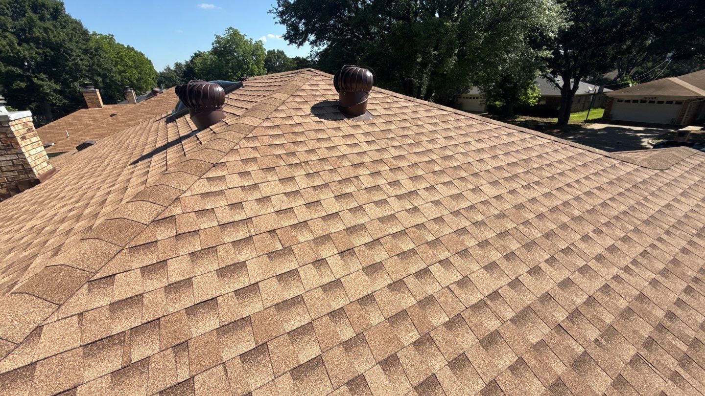 Tan shingle roof with two roof vents and trees in the background