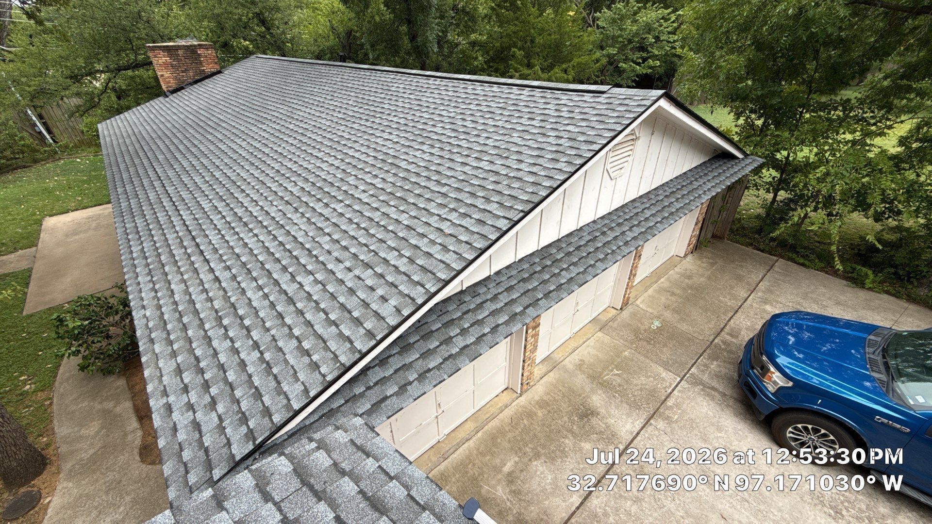 Aerial view of a house with a gray shingle roof, white siding, and a blue car in the driveway.