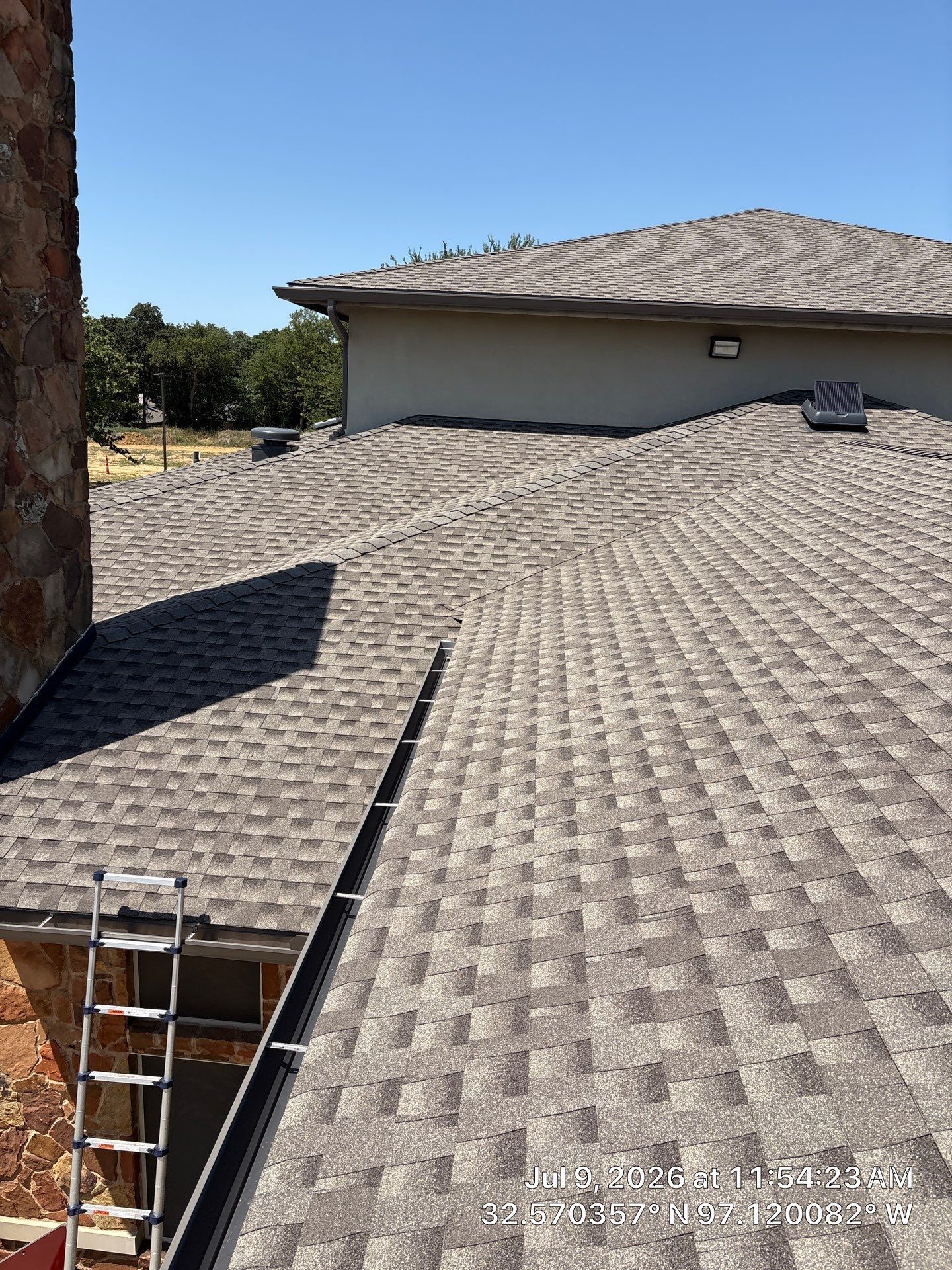 Roof under construction with gray shingles and a ladder at the lower left.
