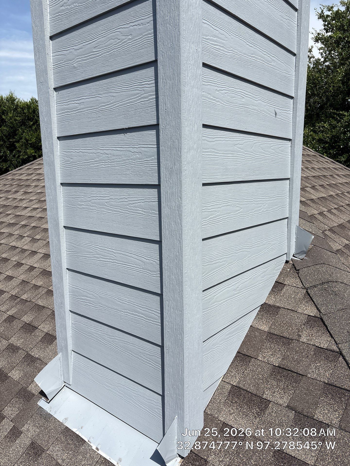 Exterior white chimney with horizontal siding on a shingled roof under a blue sky