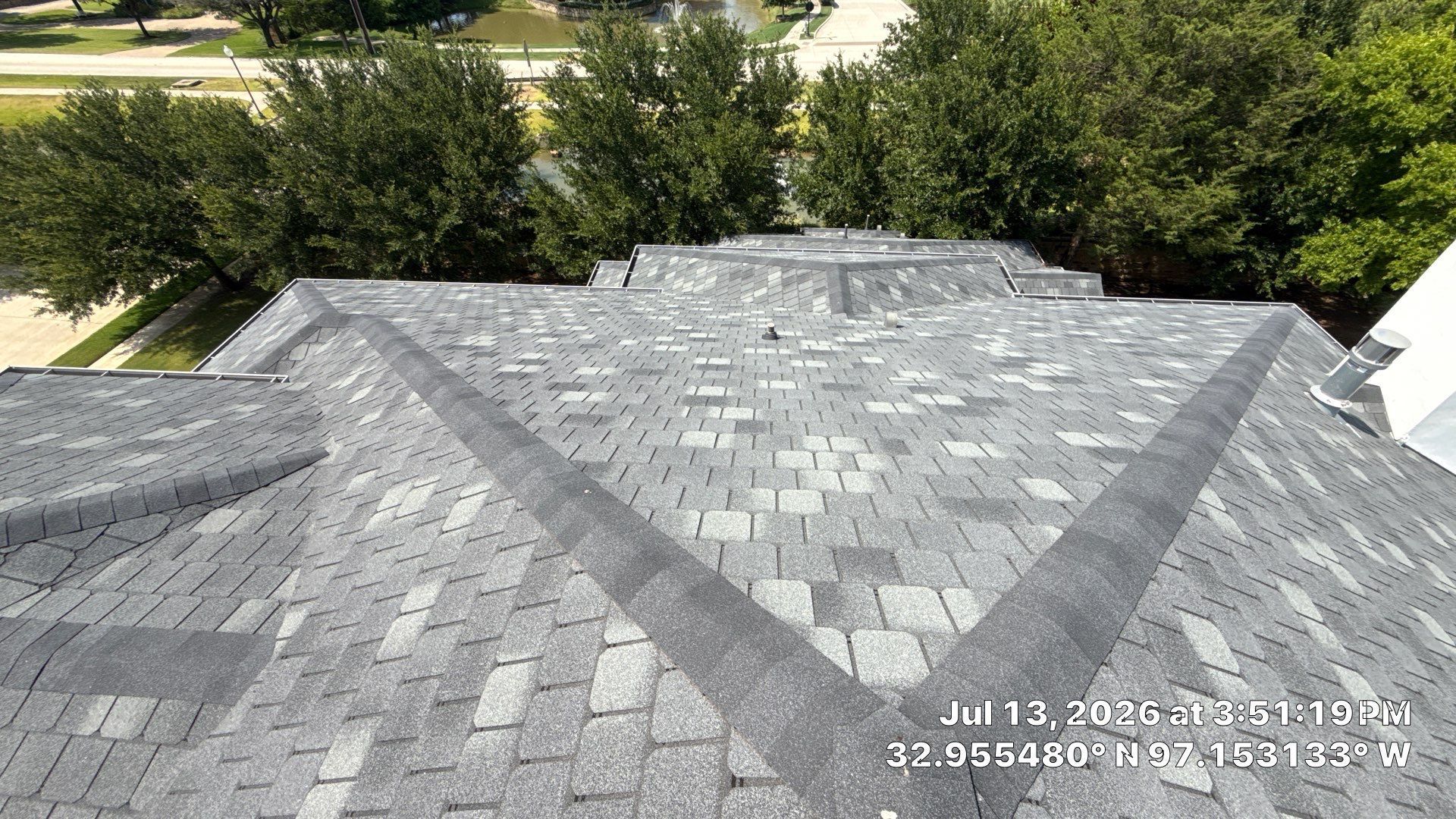 Gray shingled rooftop with trees and a road in the background