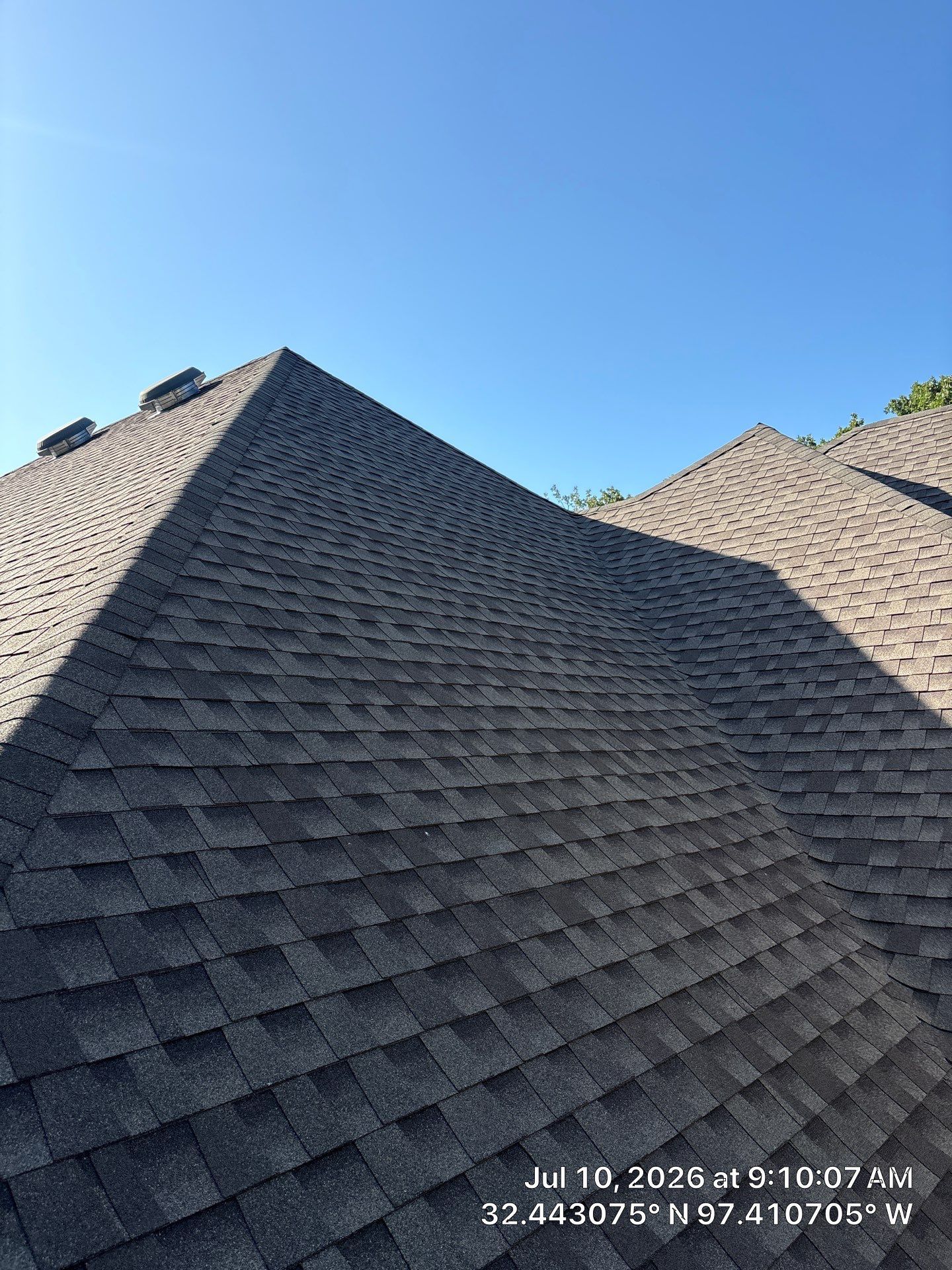 Steep gray shingled roof under a clear blue sky, with a second roof peak in the background