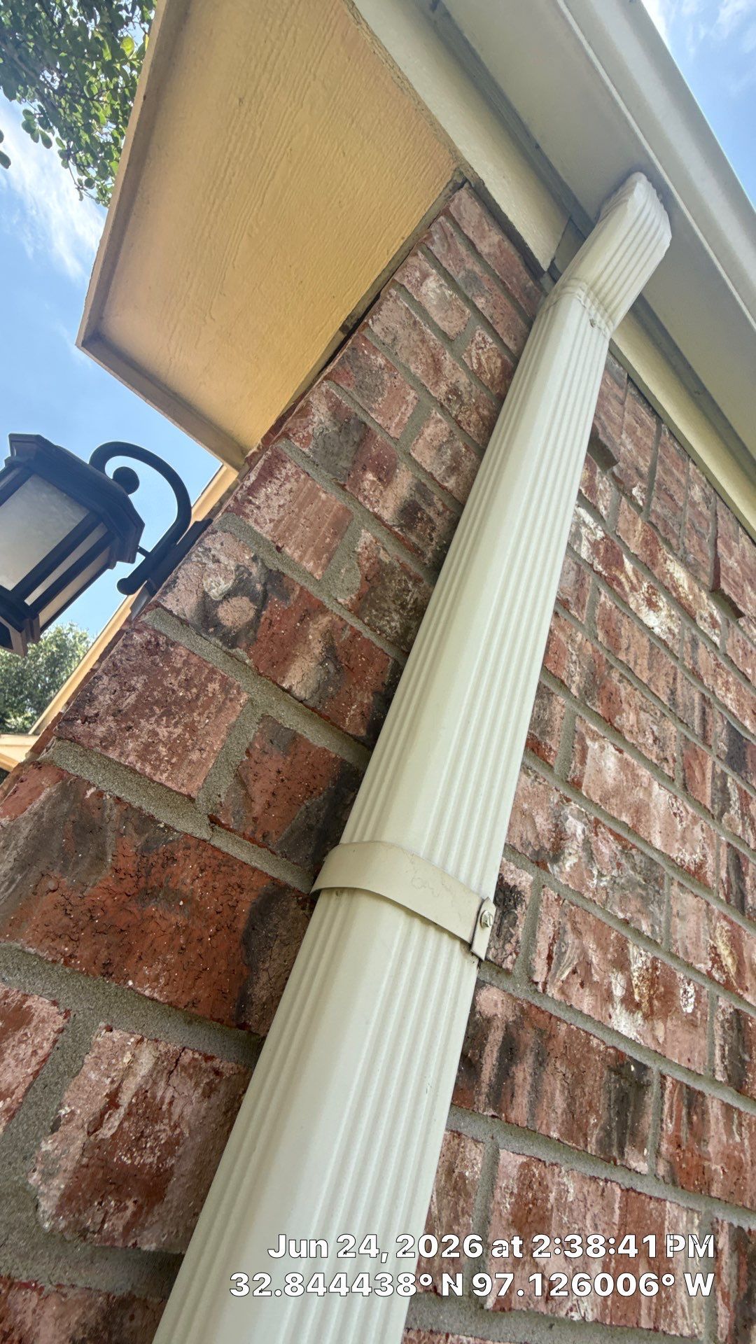 Brick house corner with cream downspout and lantern under the roof eave against a blue sky