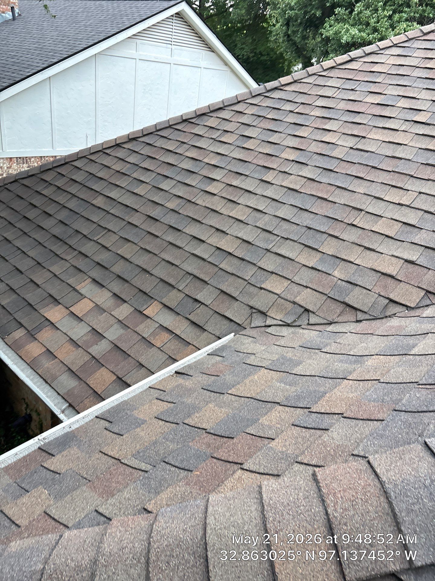 Brown shingled roof with visible wear and a white gable in the background