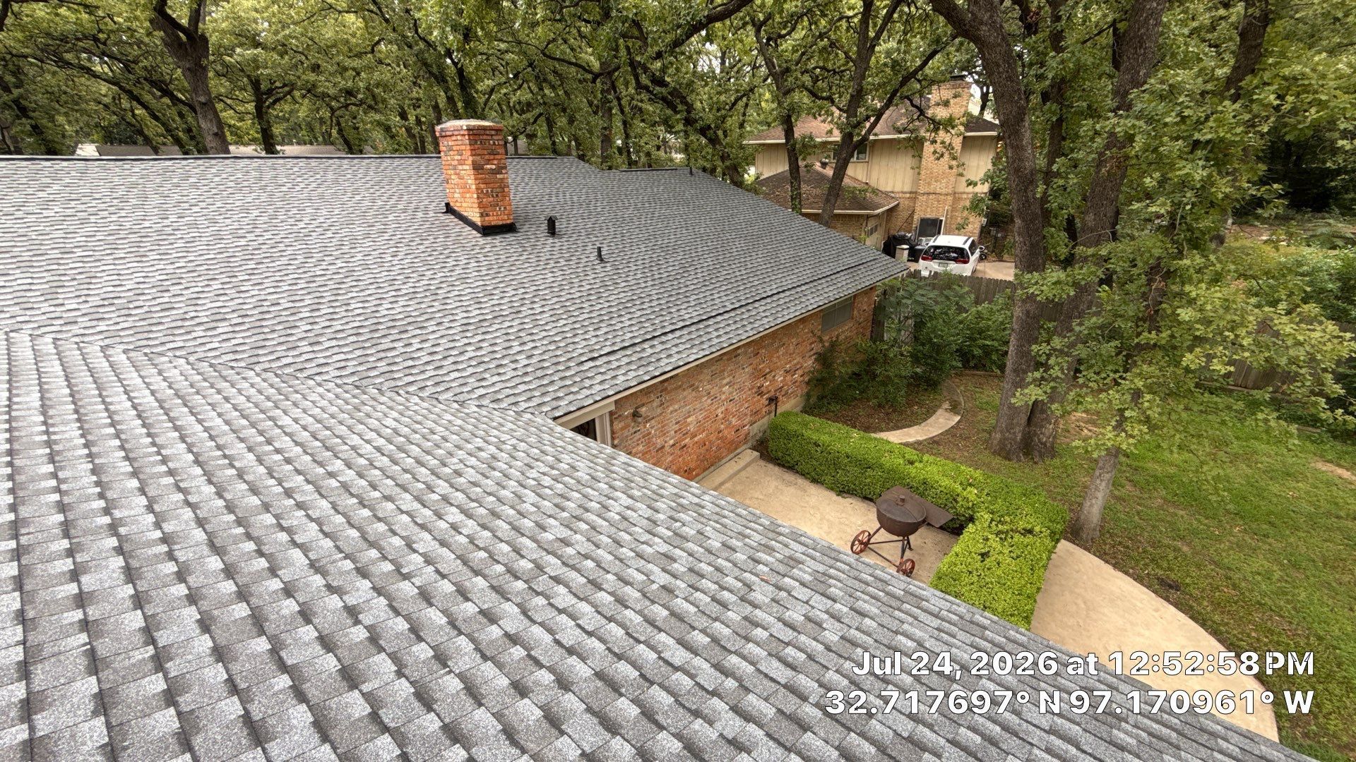 Curved gray-tiled roof on a brick building nestled among green trees and garden paths
