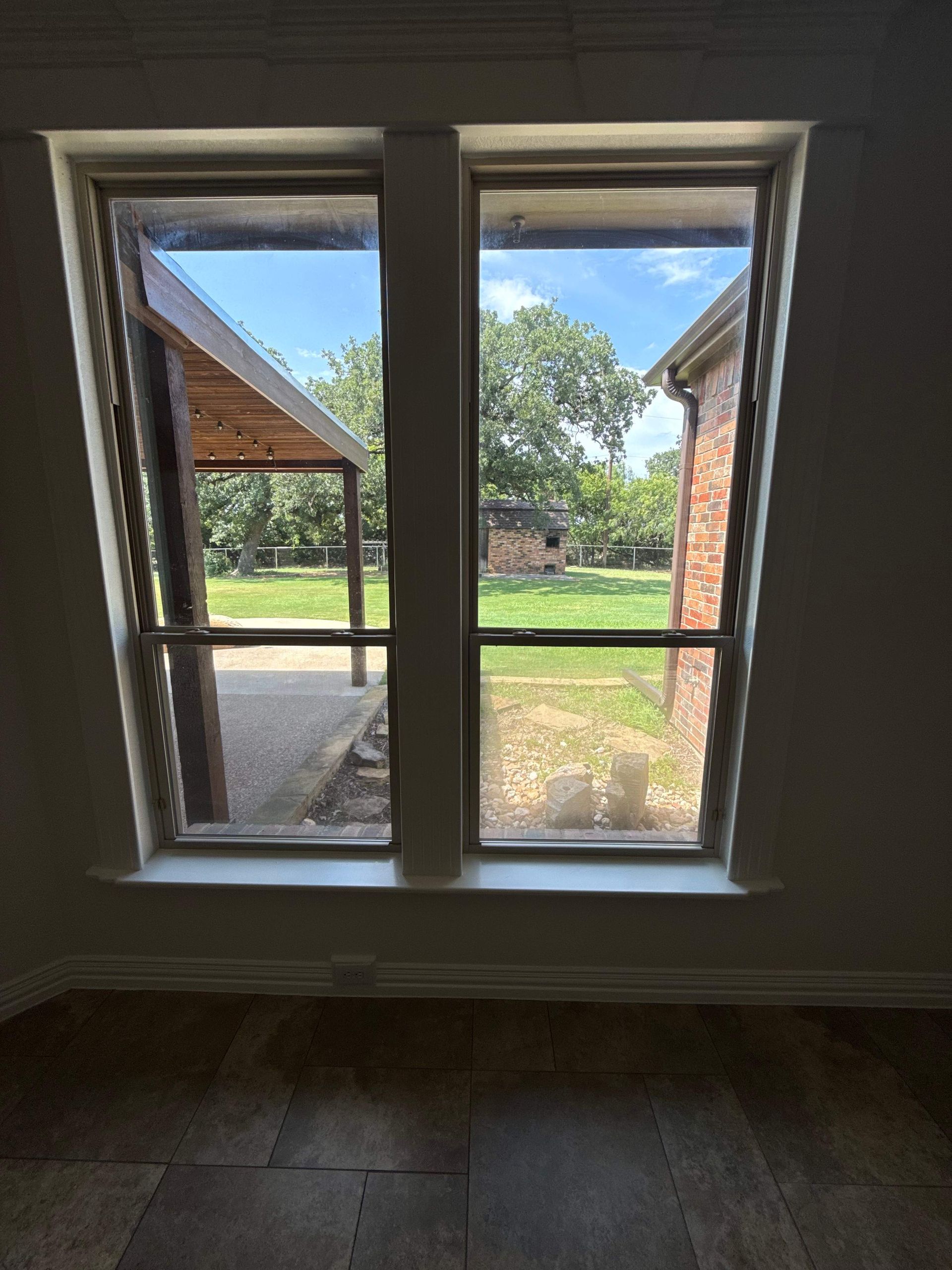 View through a white-framed window to a sunny backyard and covered patio.
