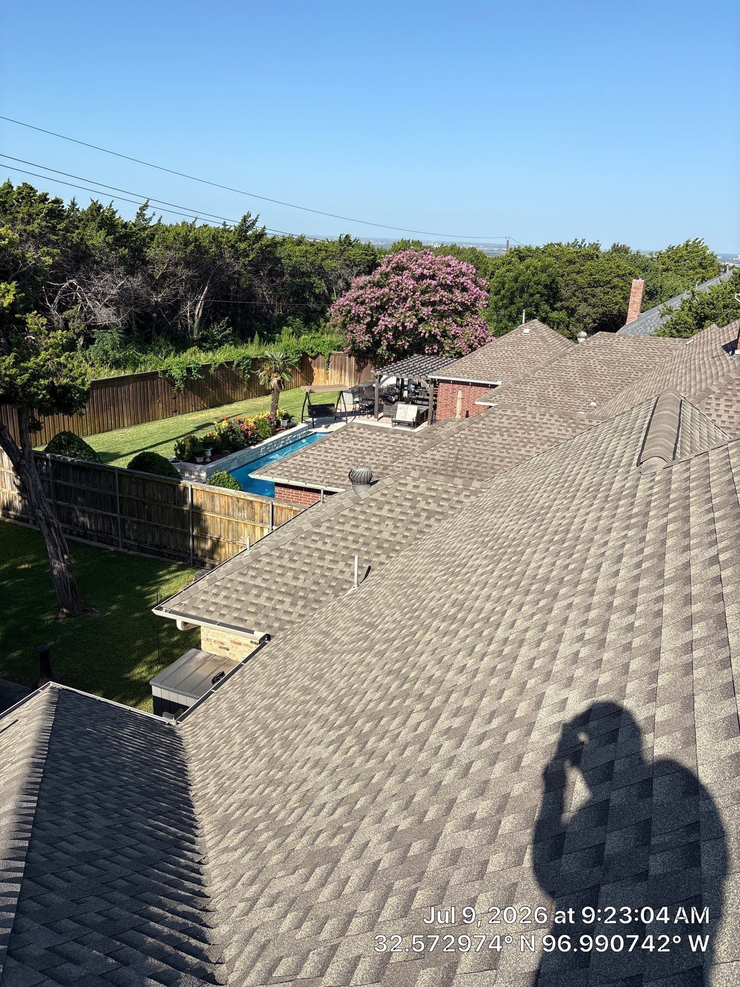 Rooftop with gray tiles overlooking a blue pool, trees, and a clear sky