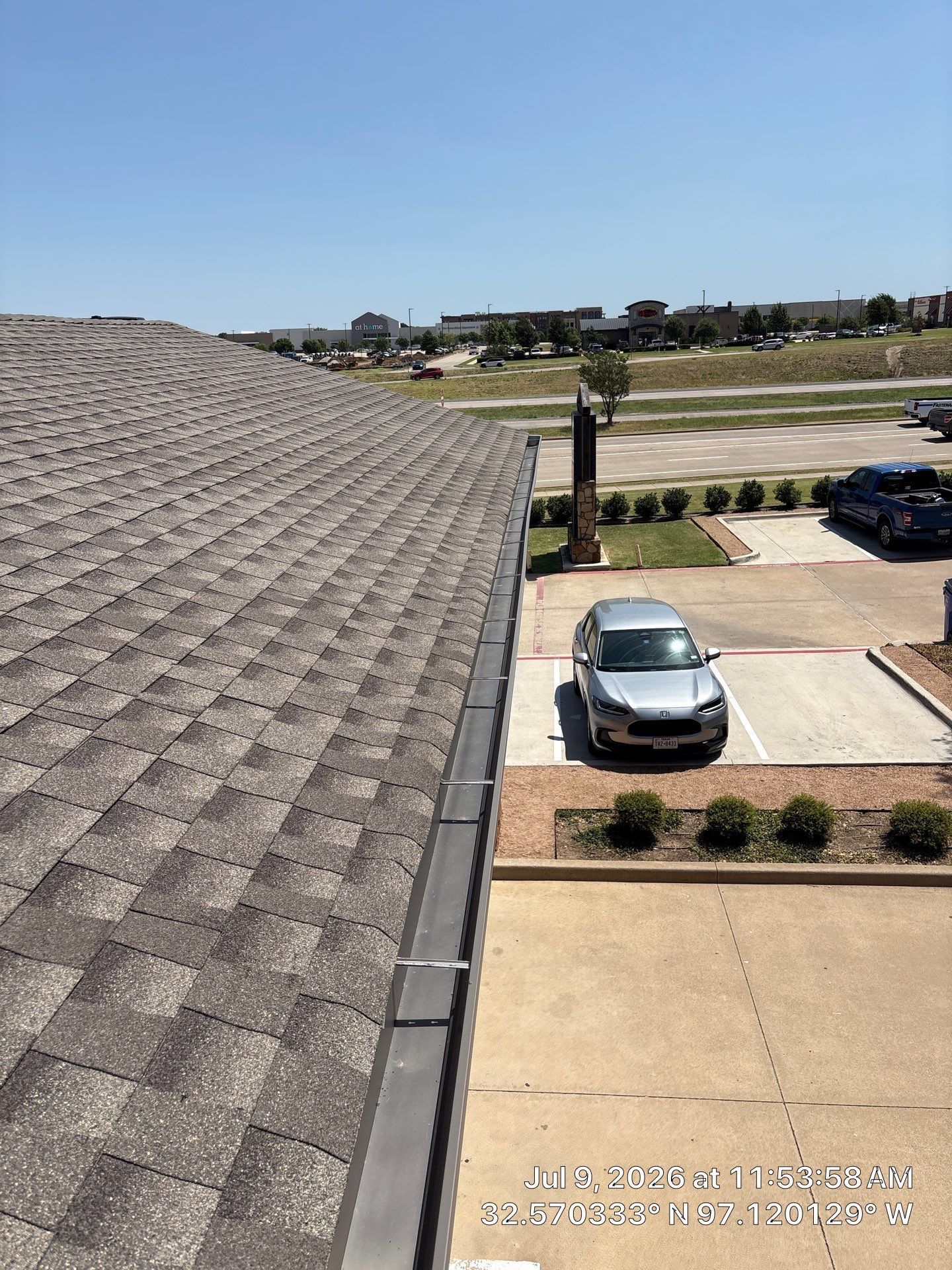 Roofline overlooking parking lot with cars, shrubs, and a clear blue sky