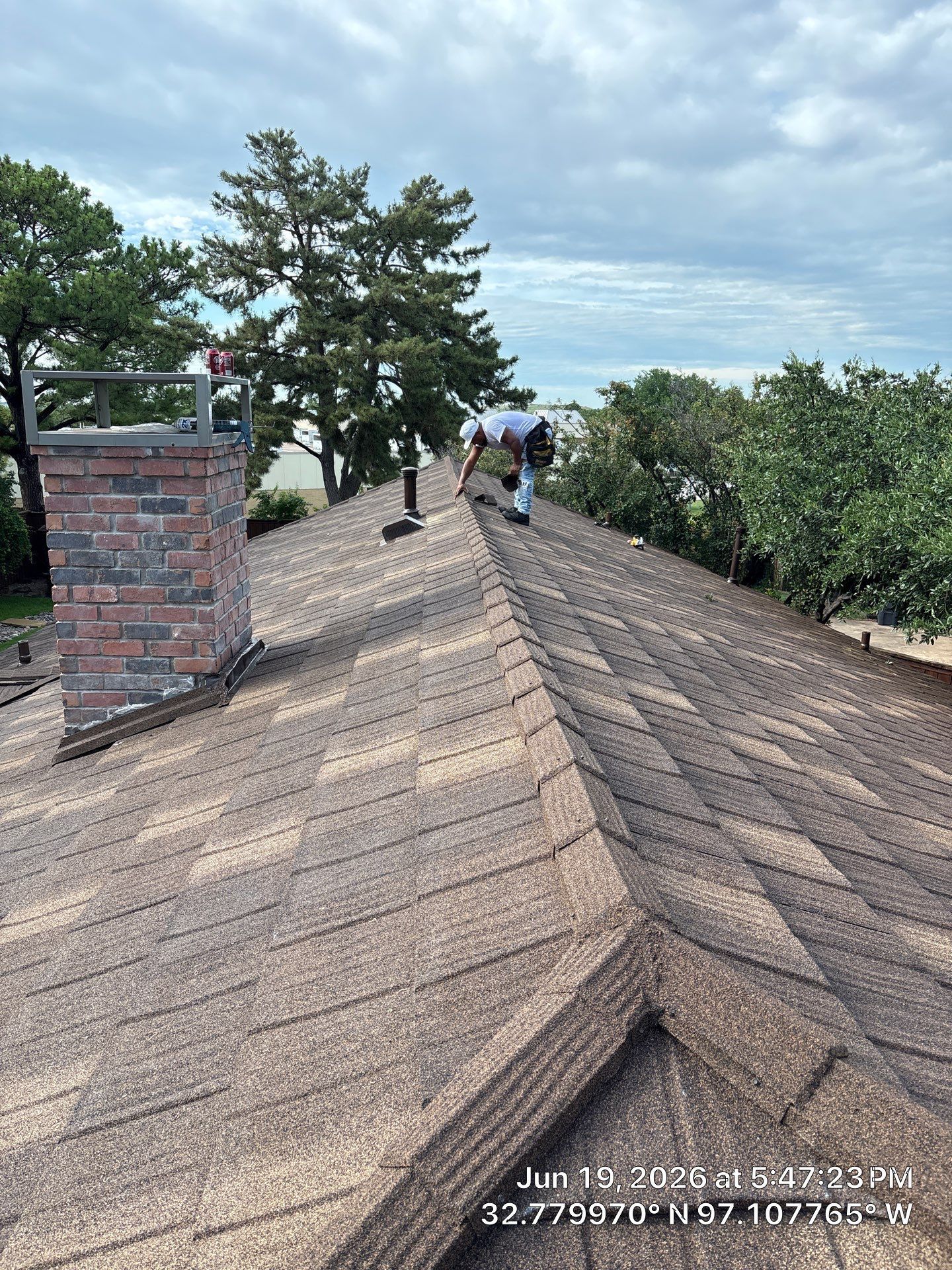 Roof ridge with two people walking, brick chimney, and trees under a cloudy sky