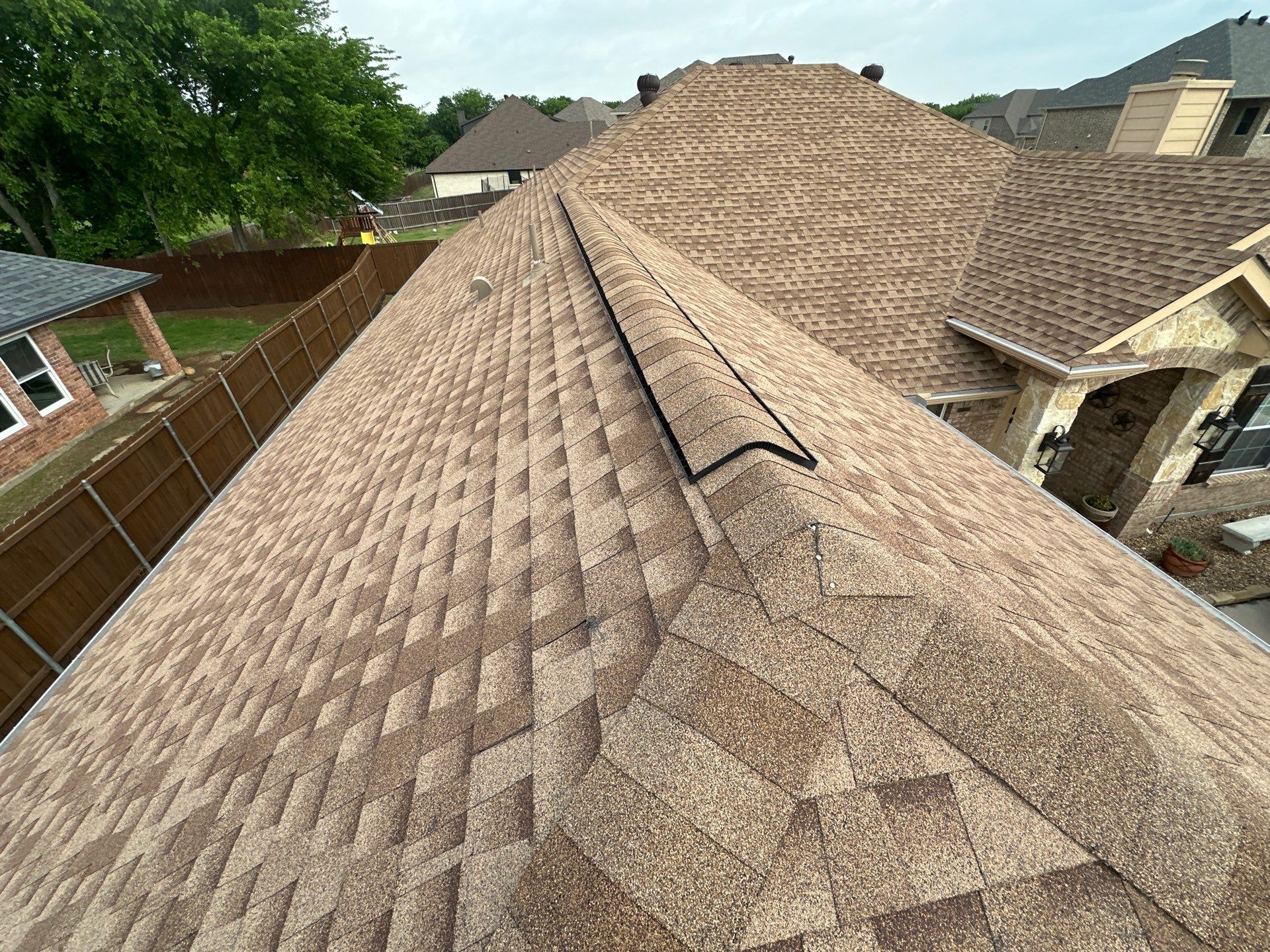 View from a shingled roof ridge in a suburban neighborhood under cloudy sky