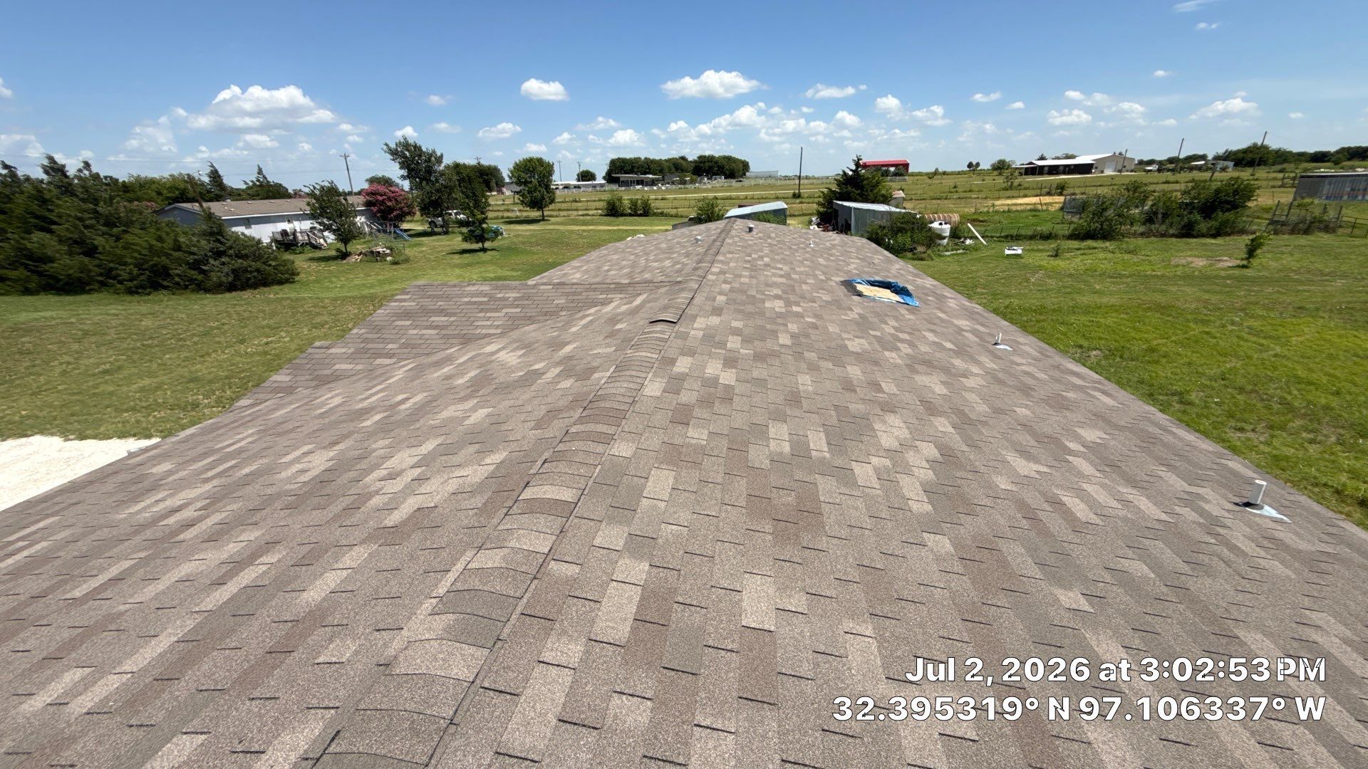 Rooftop with gray shingles overlooking a grassy field under a blue sky with clouds