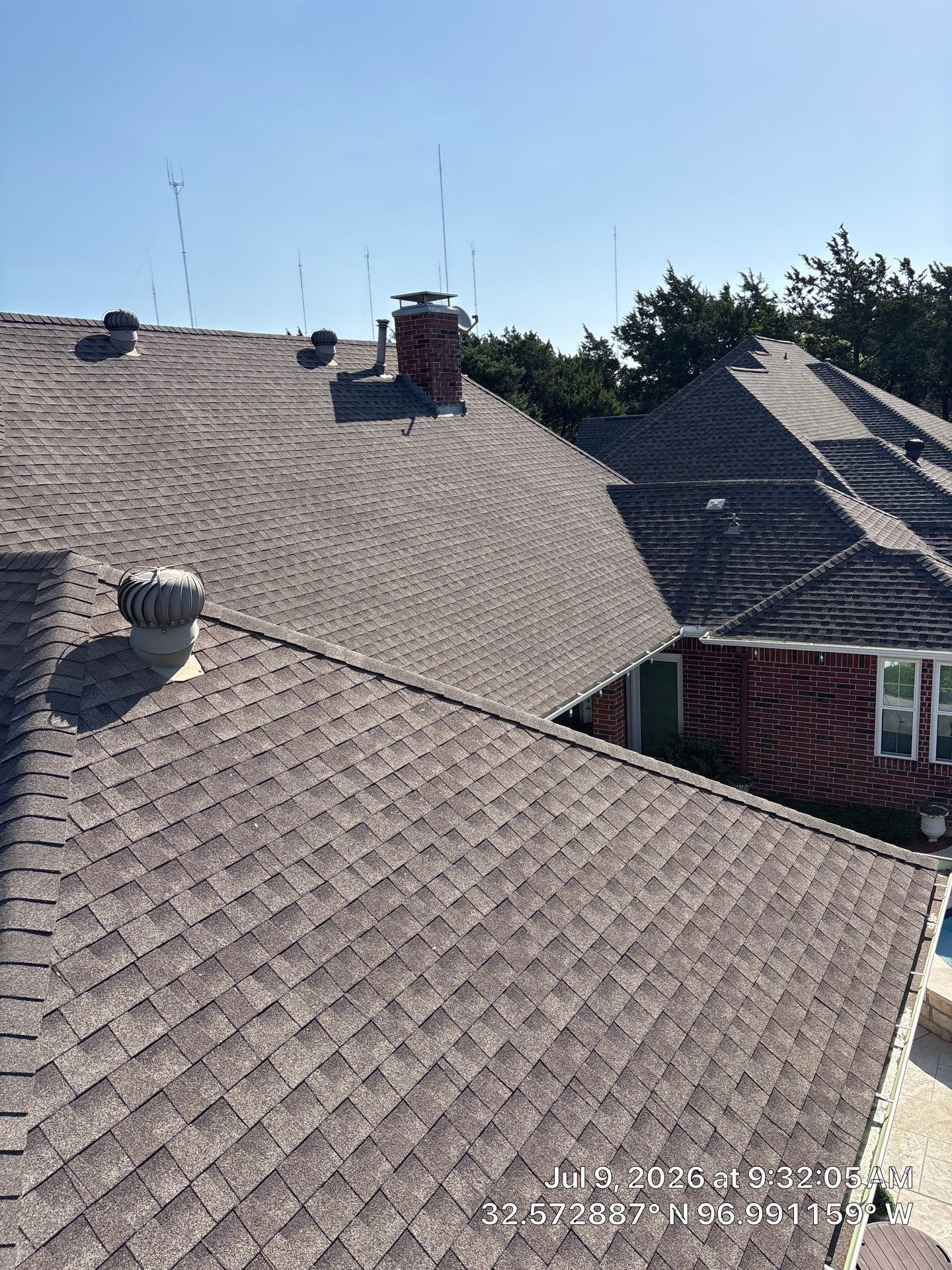 Shingled rooftops with chimneys under a clear blue sky, viewed from above.