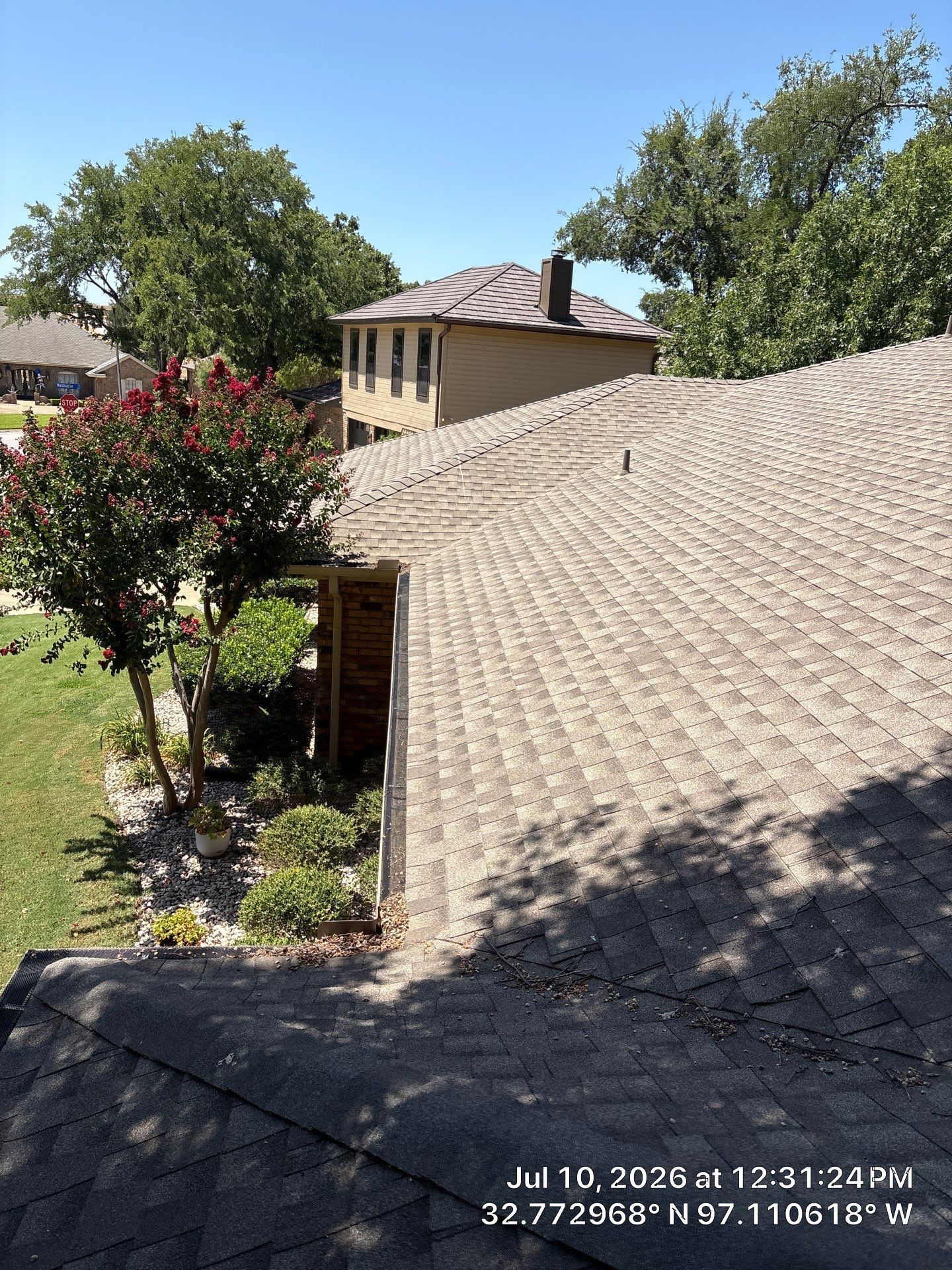 Rooftop view of a house and trees under a sunny blue sky