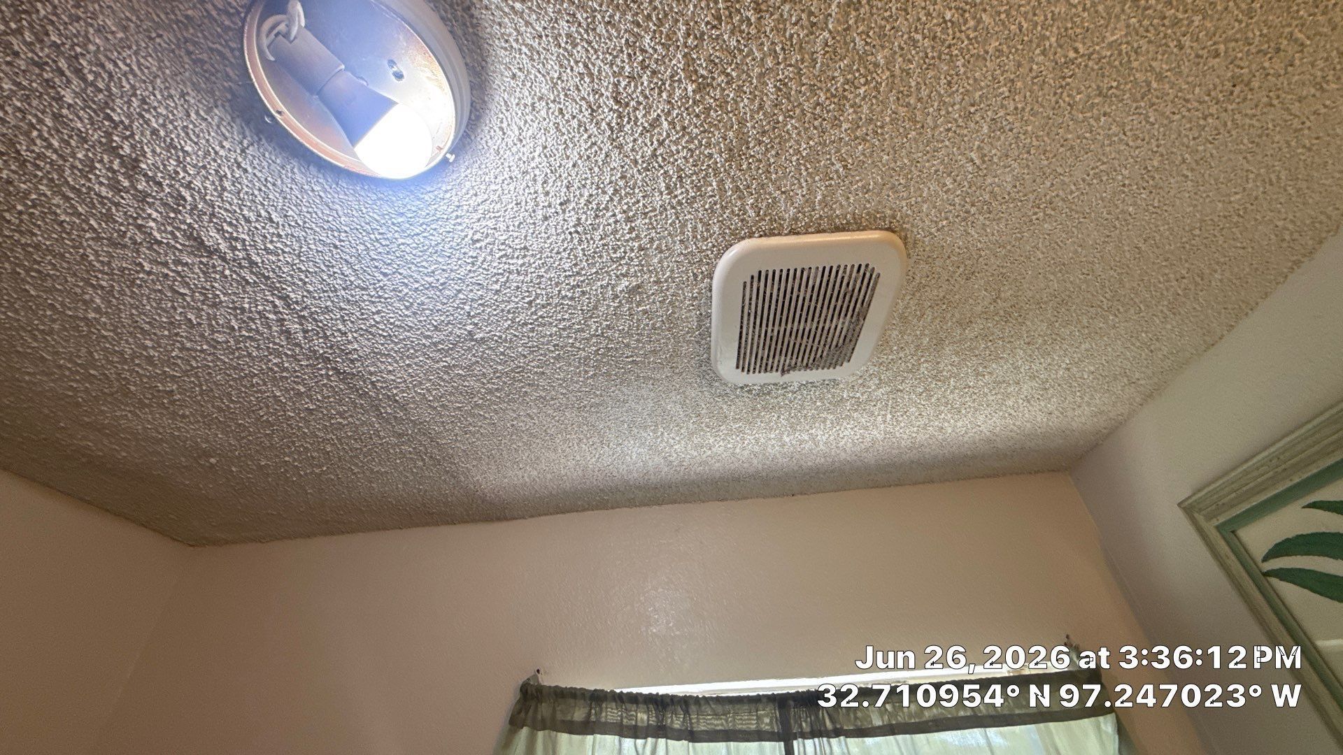 Ceiling with a lit round light, a square vent, and a window curtain below